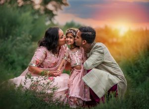 Traditional Indian dress family photoshoot mother and father kissing daughter on the cheek while the sun is setting