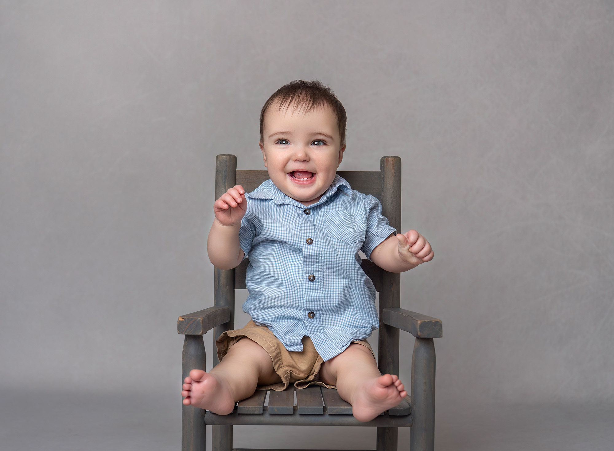 One year old boy smiling wearing blue sitting on a chair