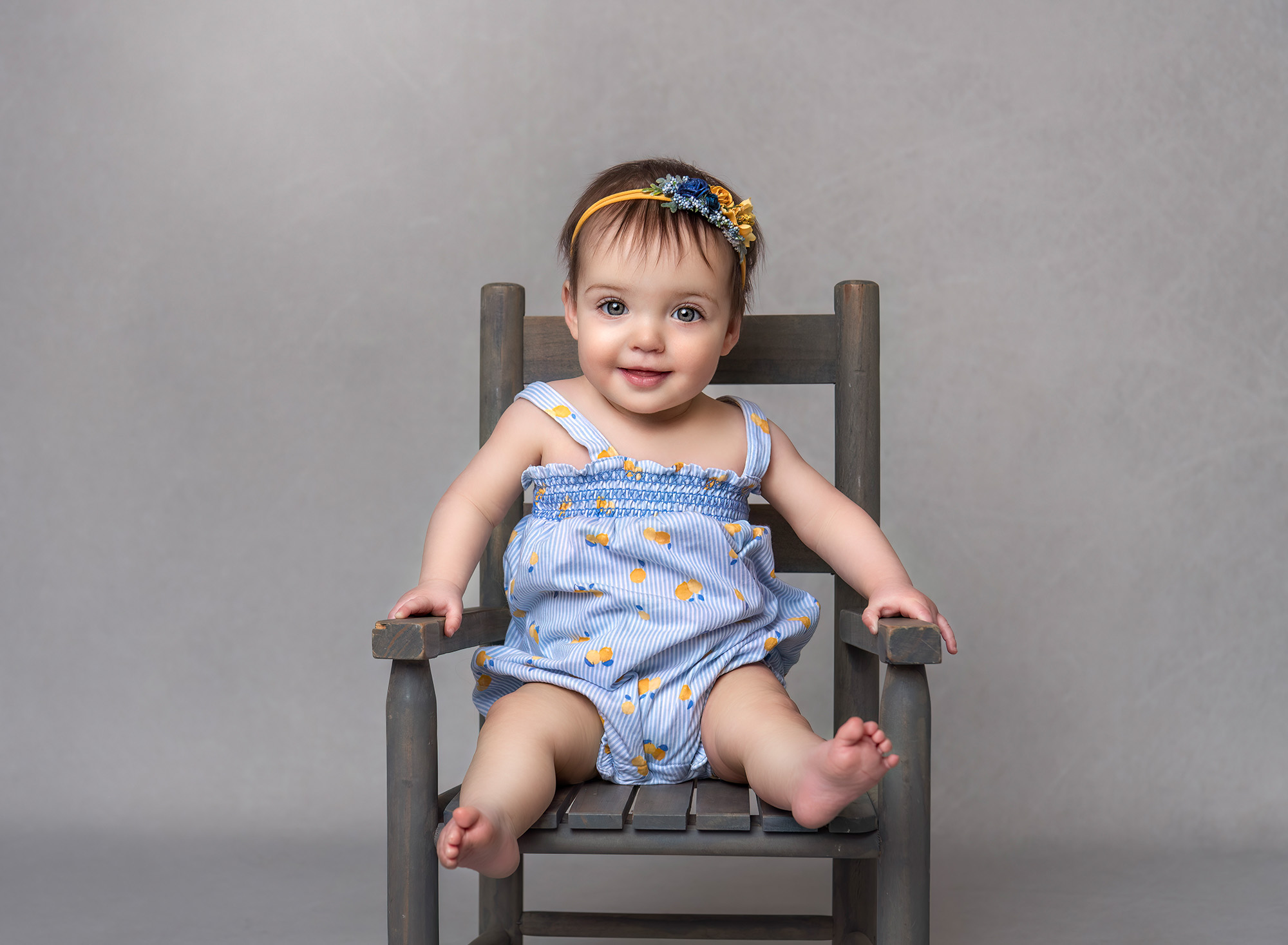 One year old girl smiling wearing blue sitting on a chair