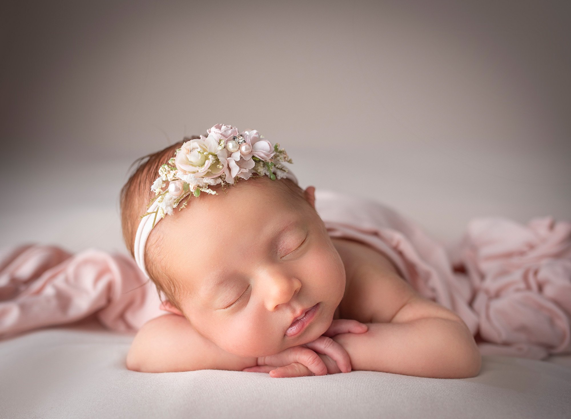 best time to take newborn photos adorable sleeping newborn baby girl with her head on her hands and her head tilted to the side and a pink floral headband 