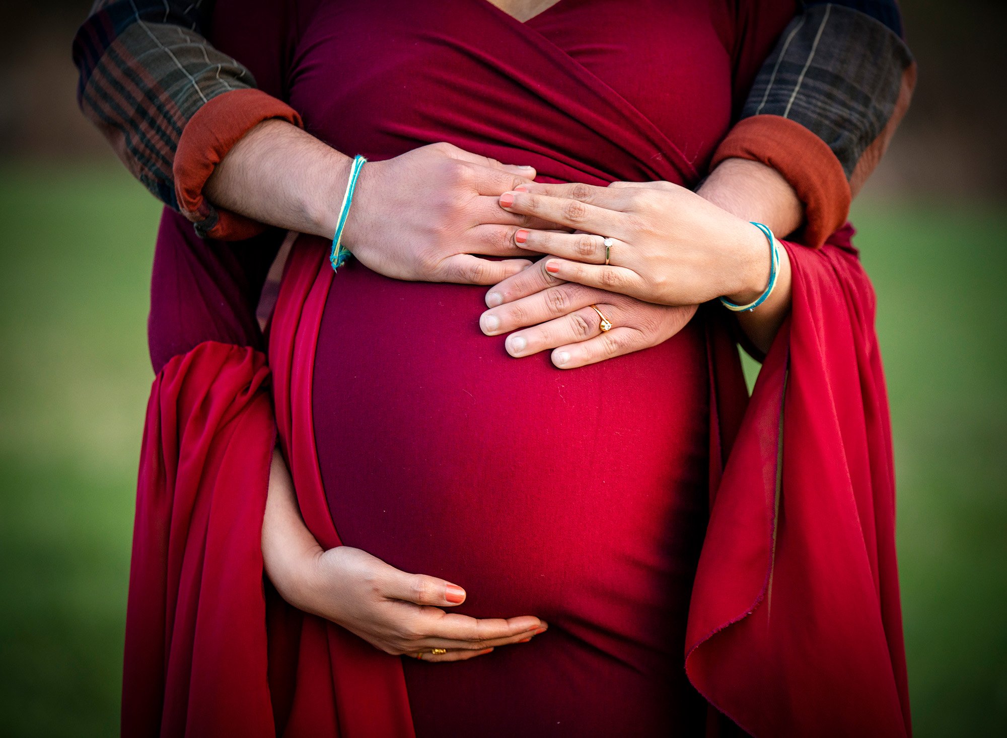 wife and partner holding hands on pregnant baby bump in red dress