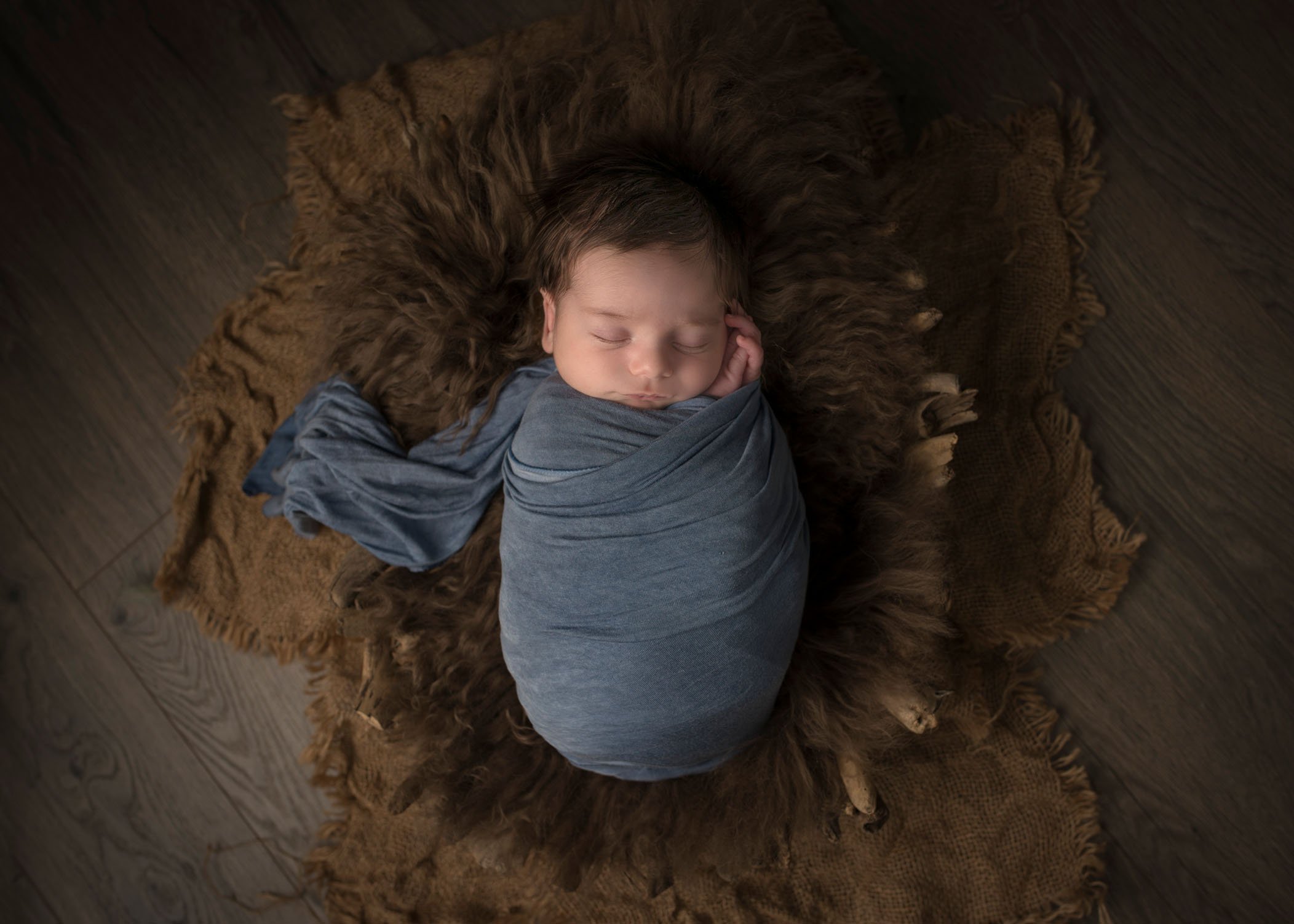 swaddled newborn boy sleeping in wooden driftwood bowl