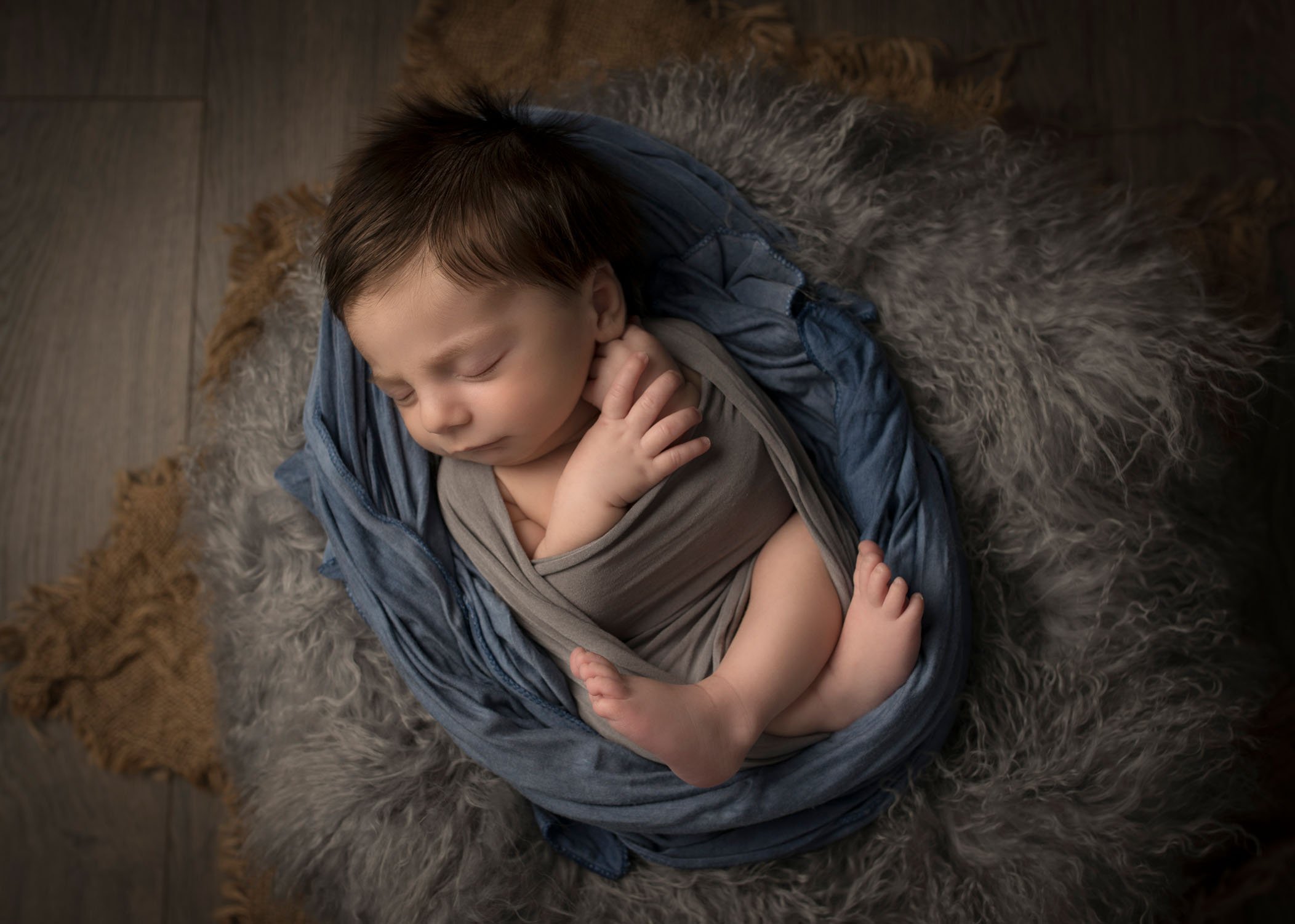 newborn baby boy wrapped in grey and blue swaddling sleeping on grey fur