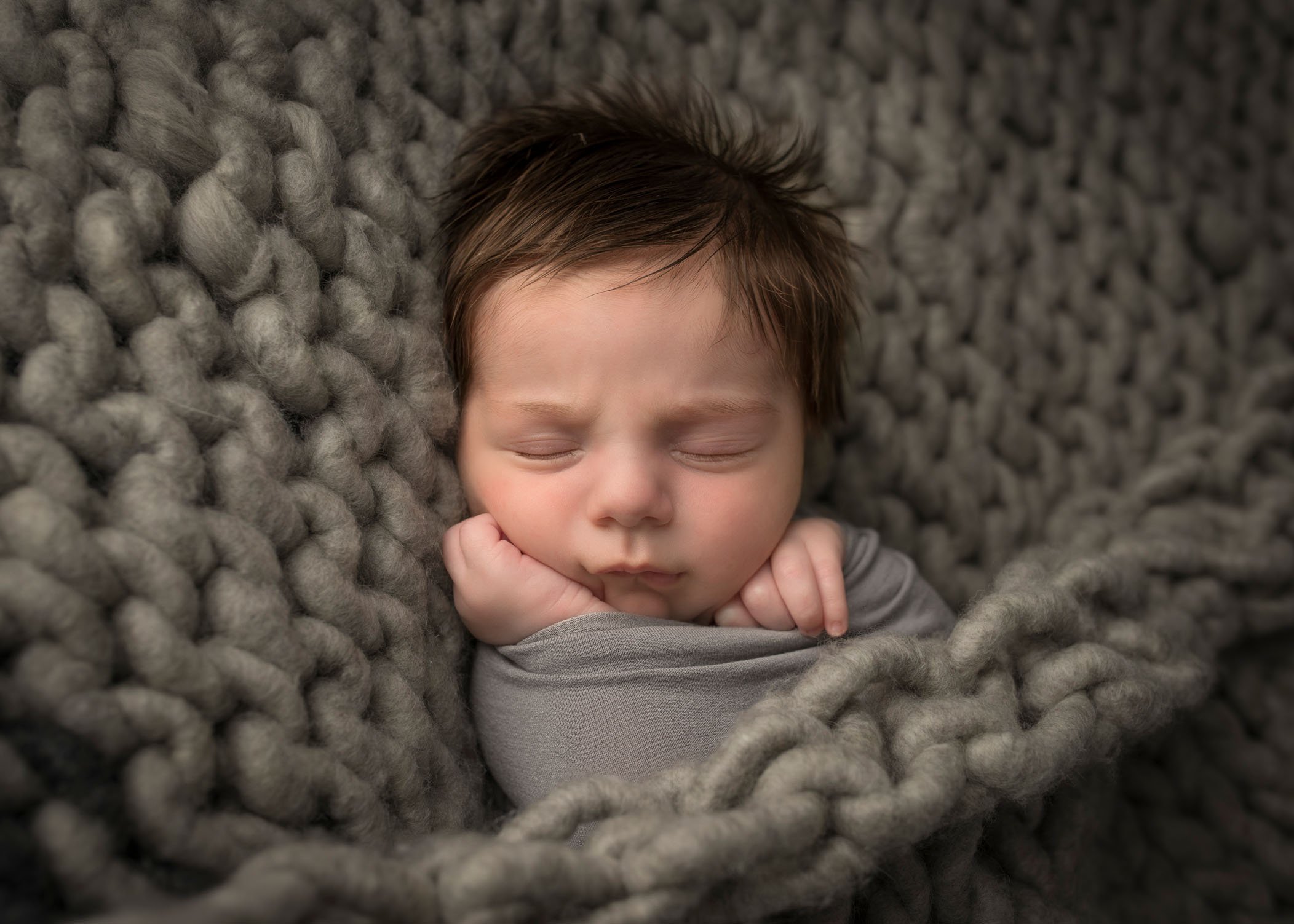newborn baby boy asleep in grey chunky knit blanket