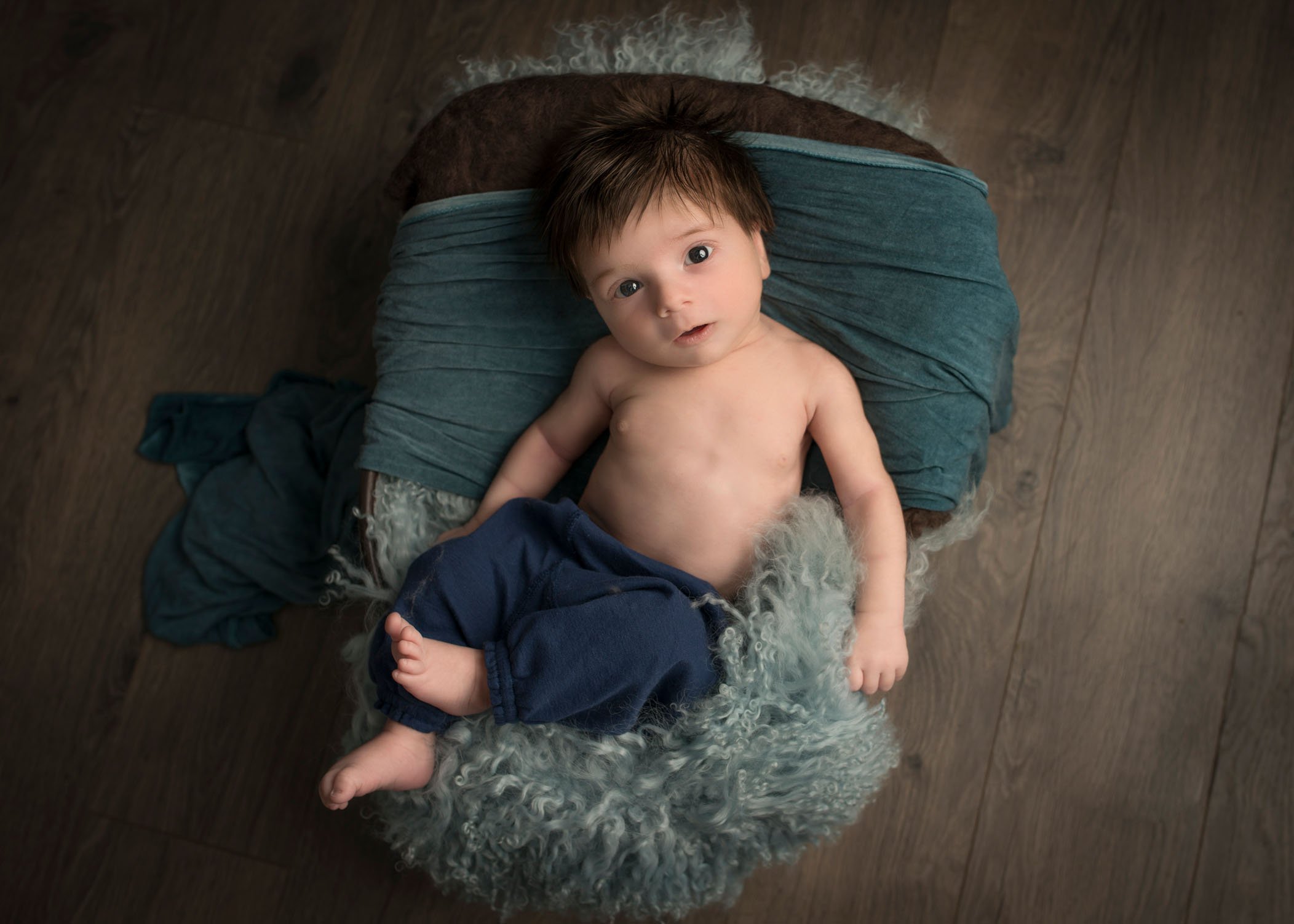 newborn boy lying on fur pallet with pants on and looking at camera