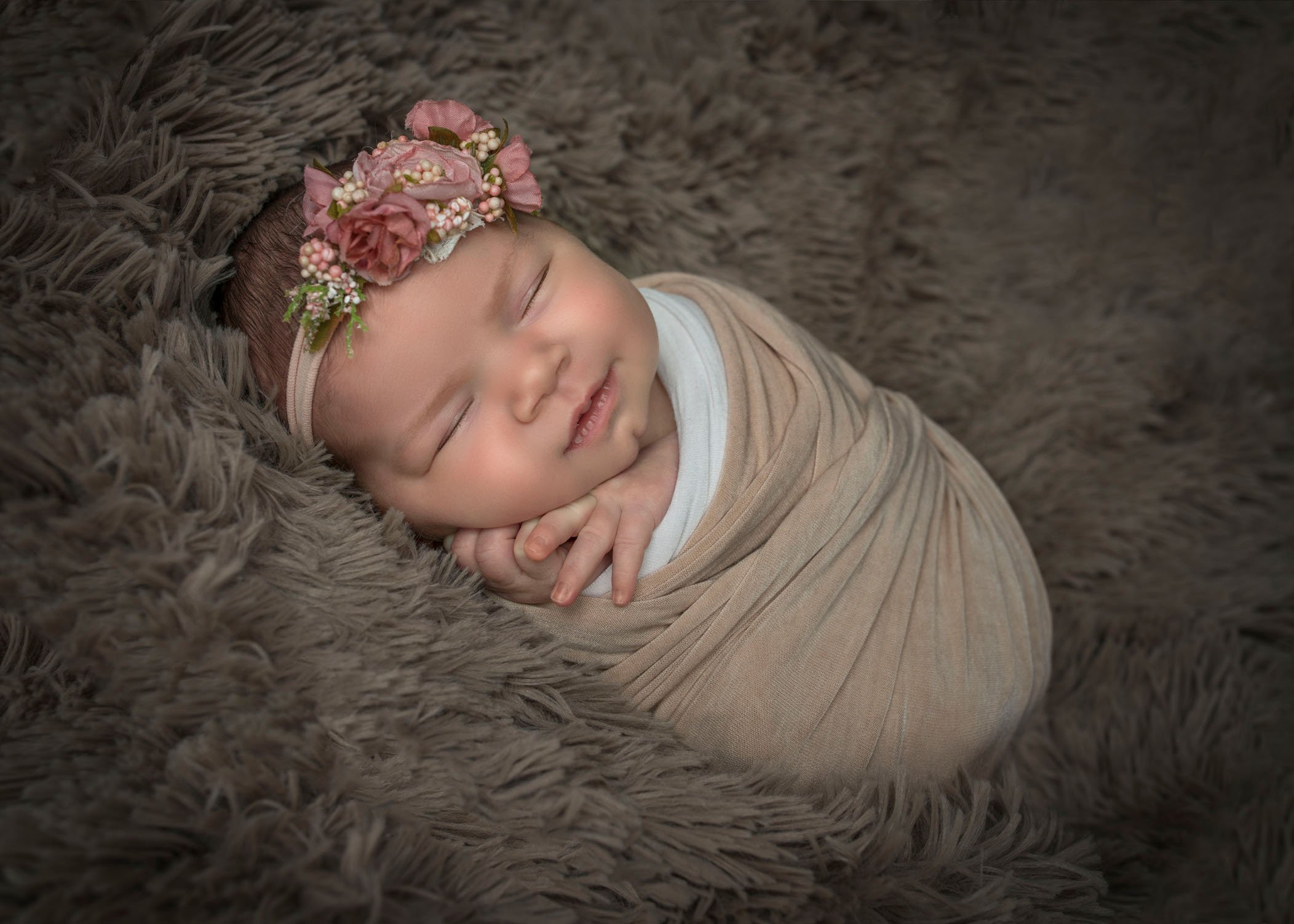 newborn baby girl wrapped up sleeping on brown fur smiling