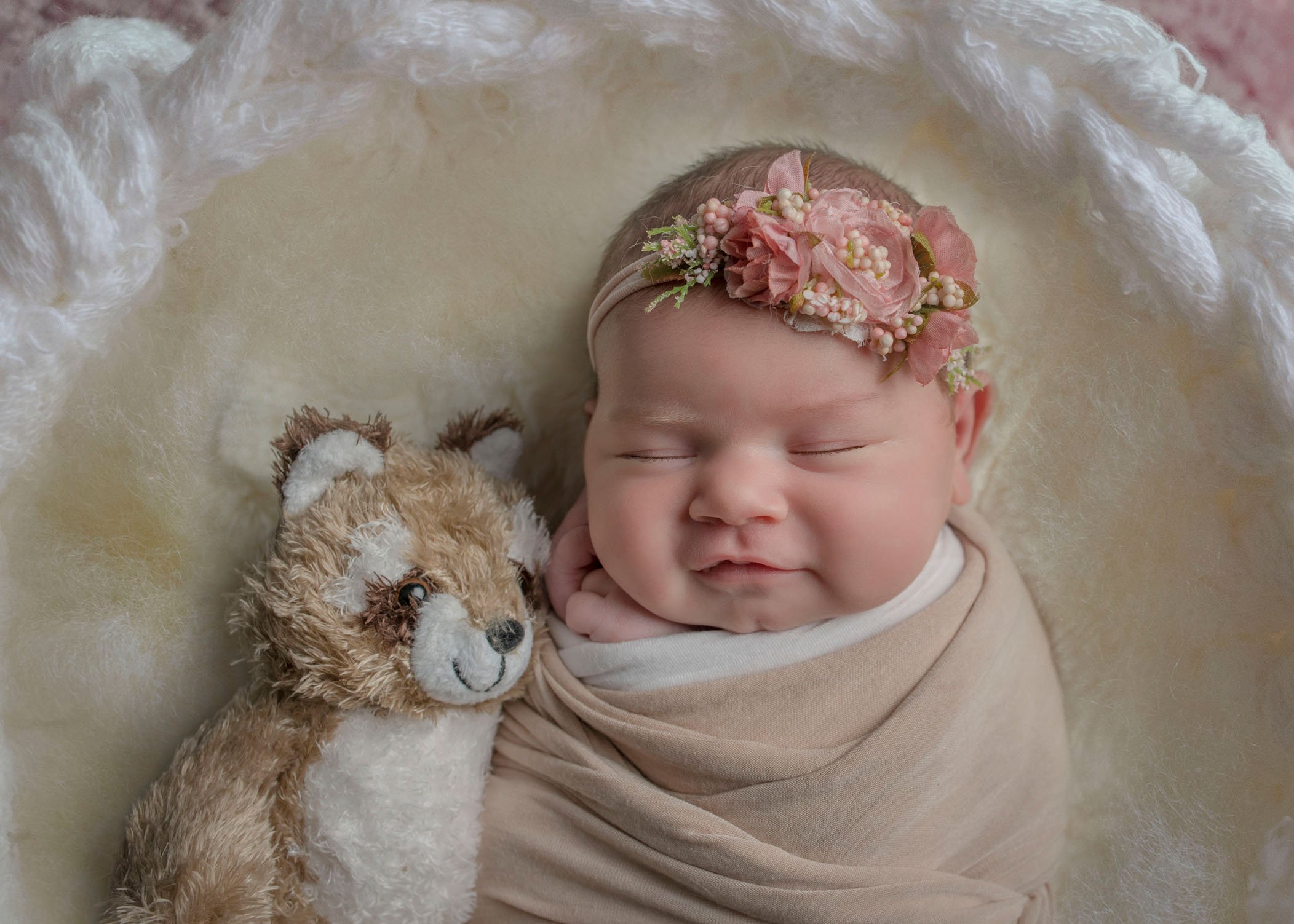 newborn baby girl smiling while sleeping with stuffed toy racoon