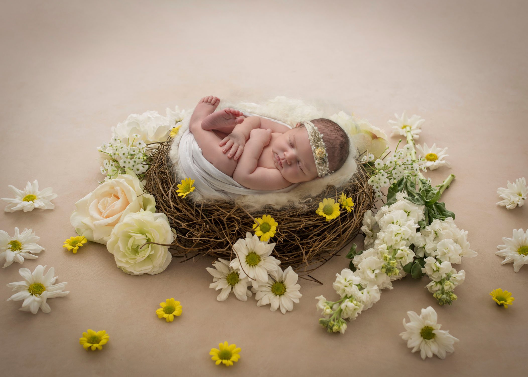 newborn baby girl sleeping in grape vine wreath surrounded by scattered spring flowers