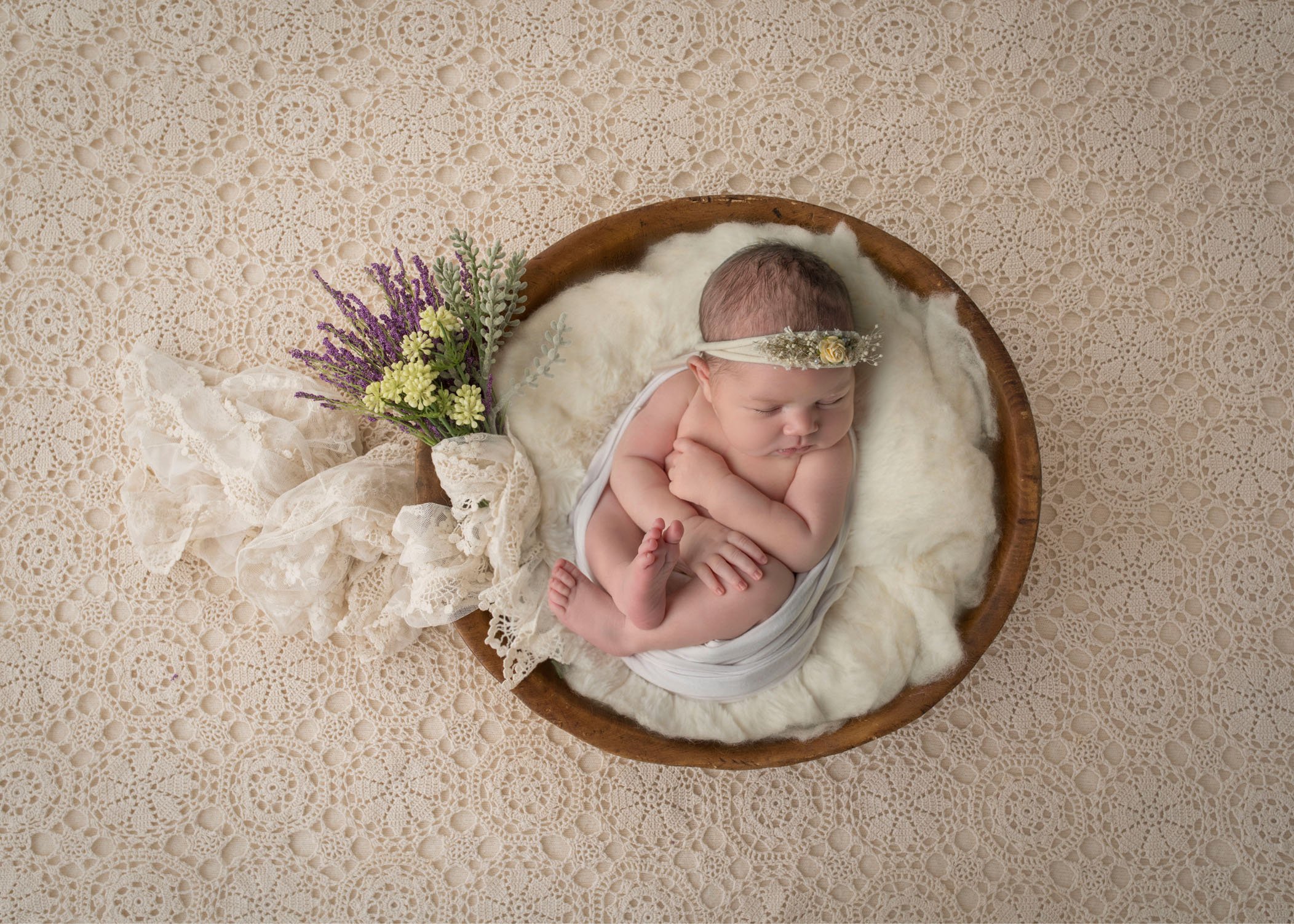newborn baby girl asleep in wooden bowl with flowers nearby