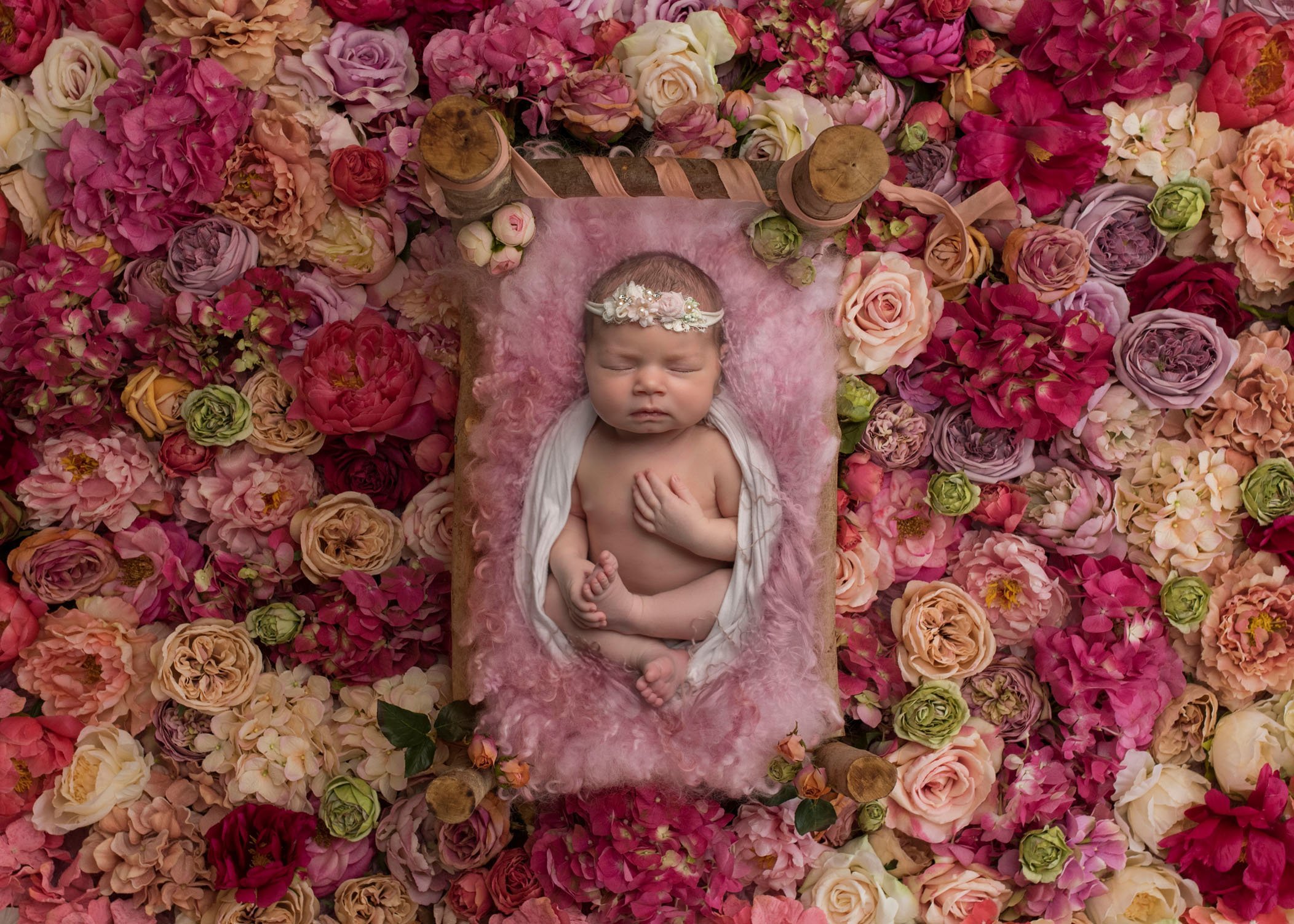 newborn baby girl asleep on bed in the middle of tons of pastel colored roses