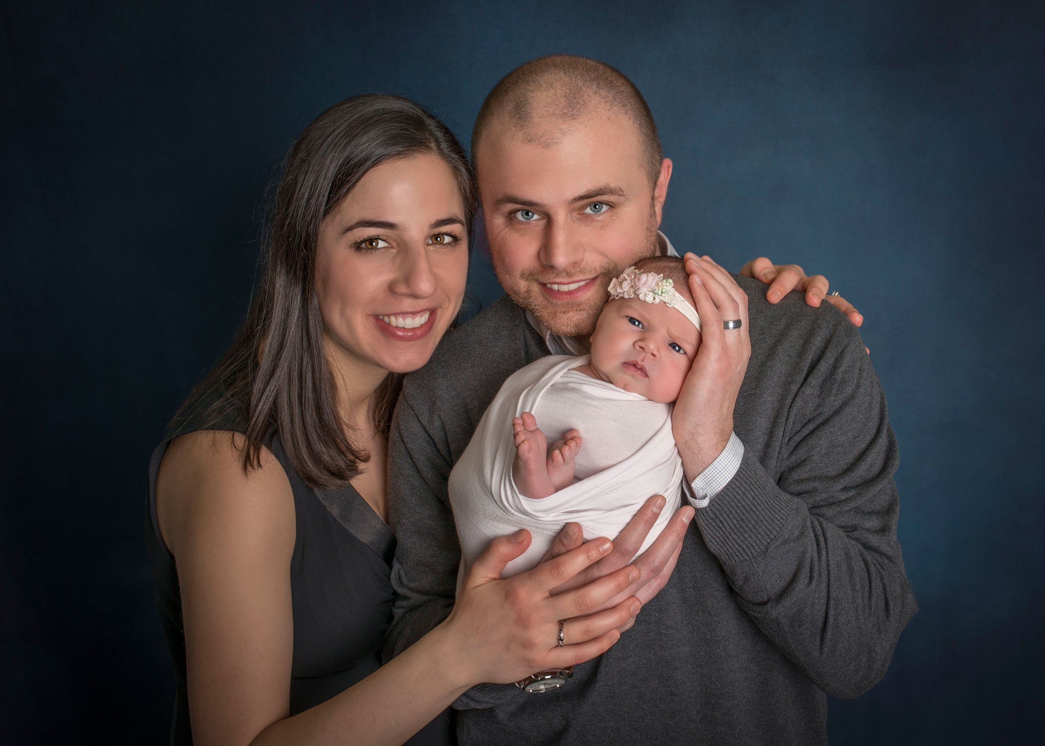 Mom and Dad holding newborn daughter in their hands looking at camera