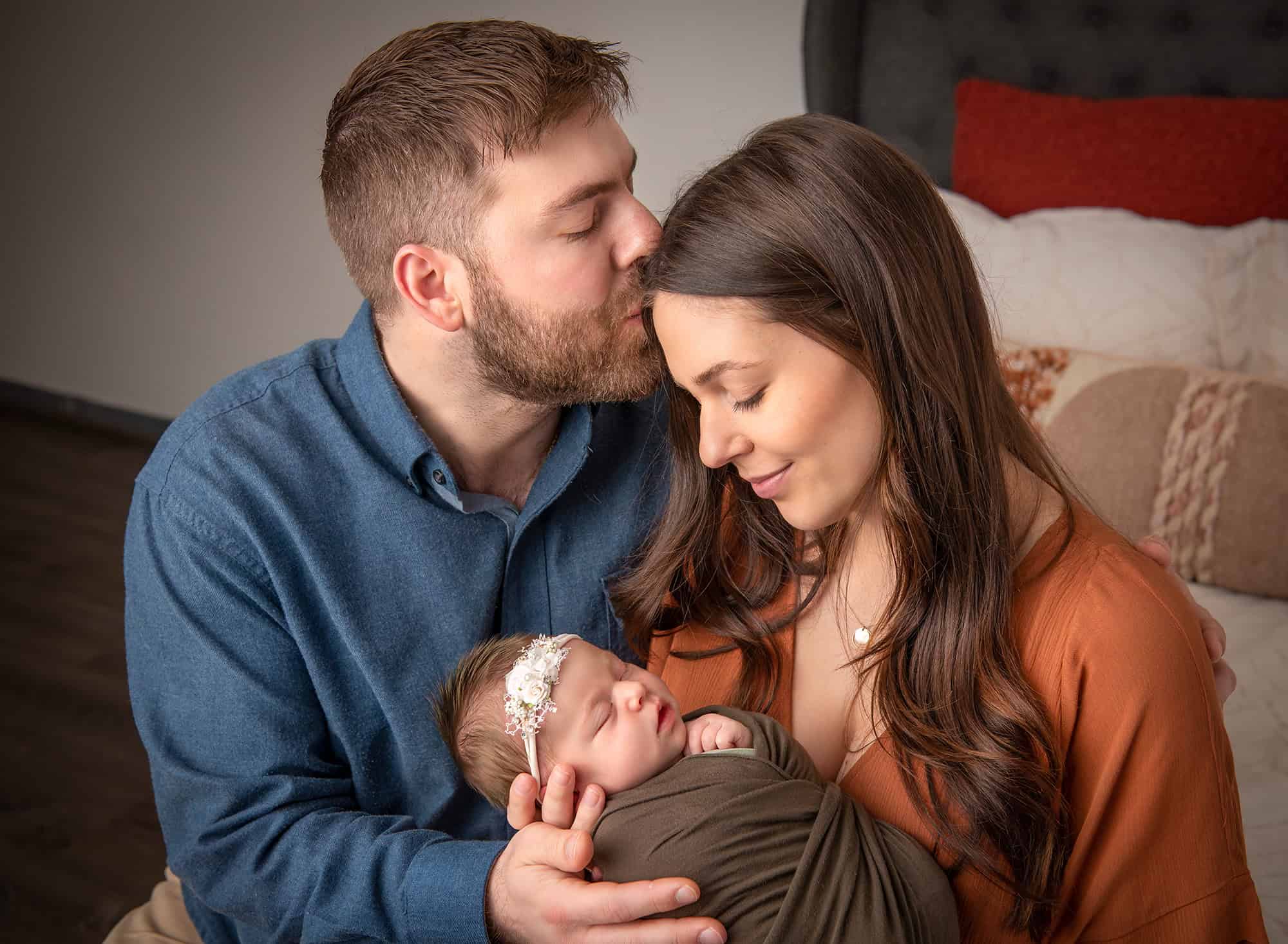 parents in newborn photos dad kissing mom's head while she lovingly gazes down at their new daughter