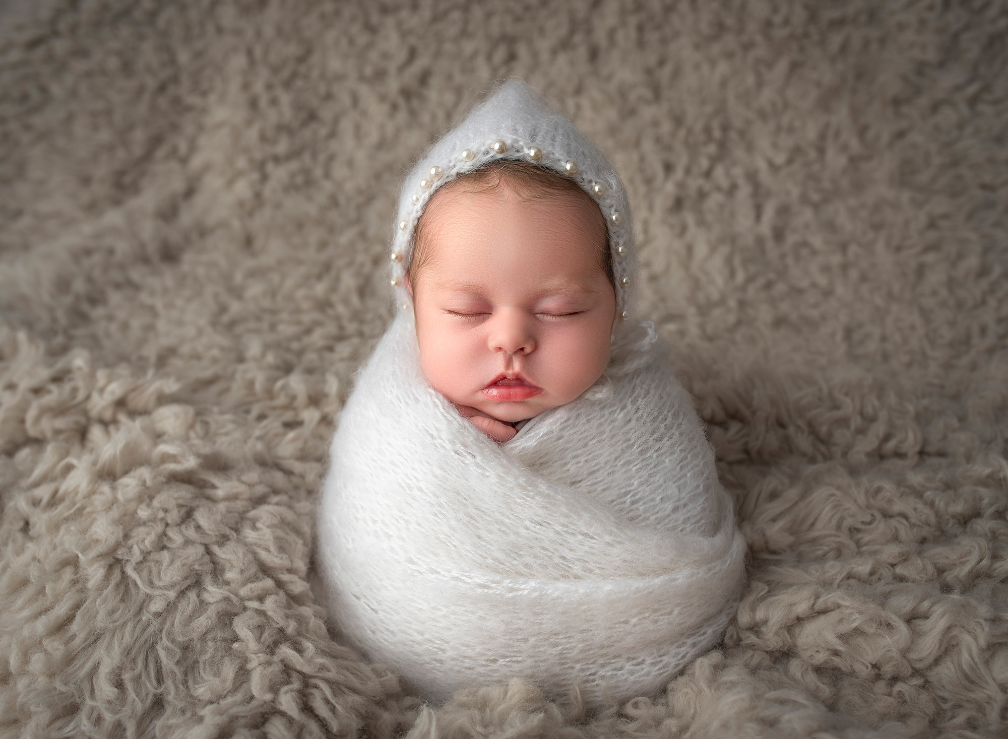 newborn baby wrapped in white sleeping wearing a pearl bonnet