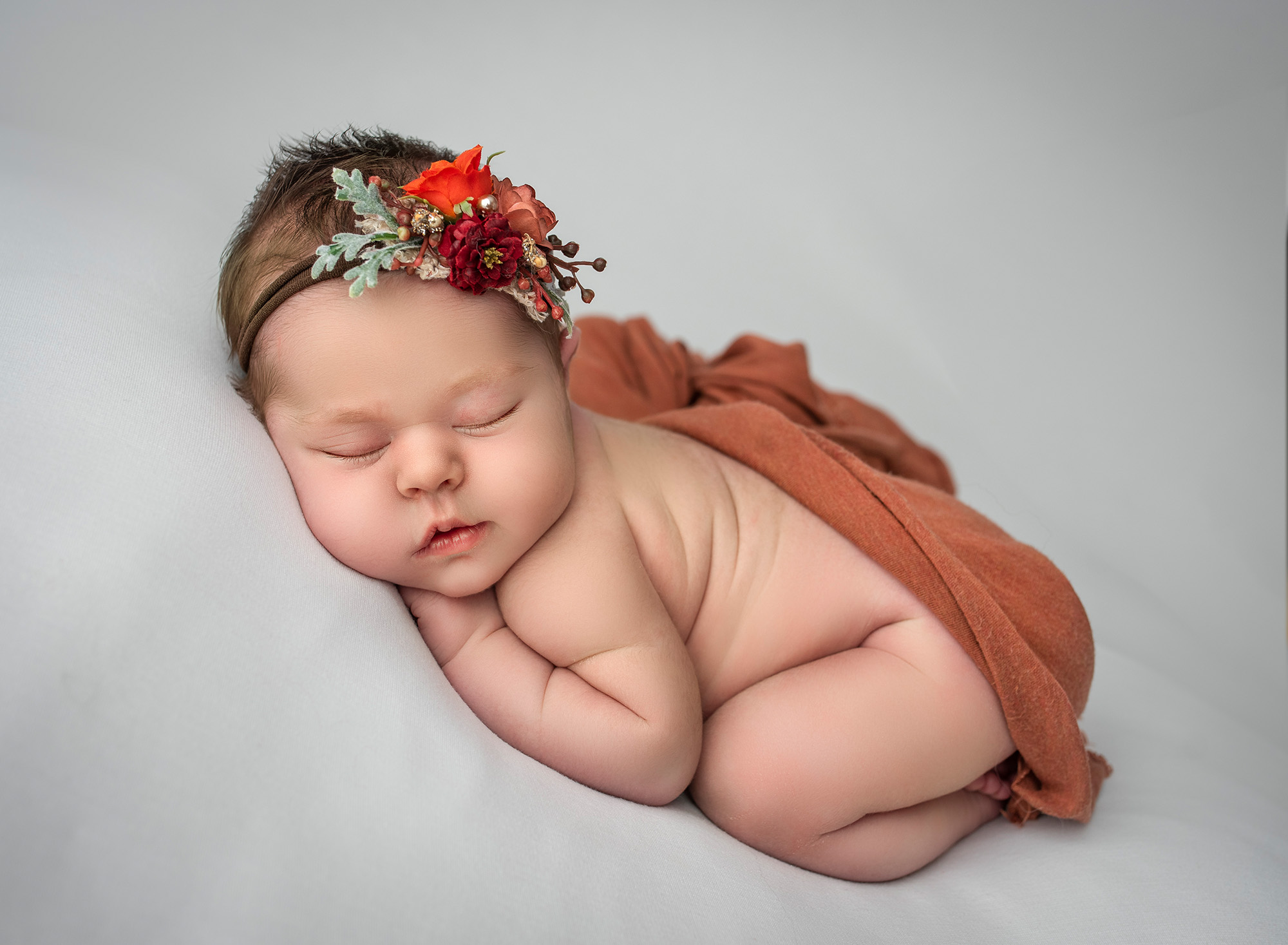 best newborn photography A newborn baby girl peacefully sleeps on a white cloth, surrounded by soft lighting, with her hand gently cradling her cheek