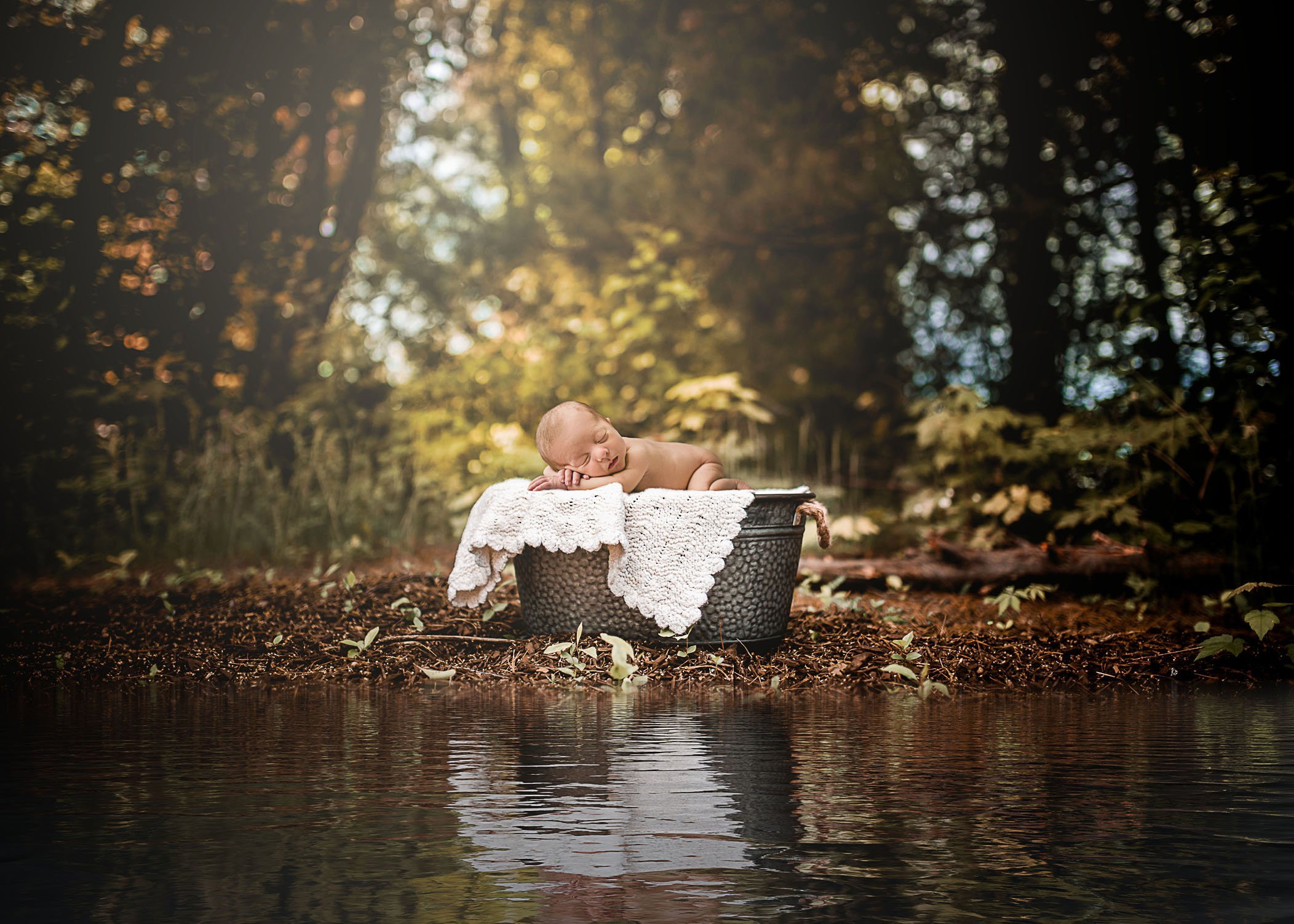 Newborn baby sleeping in a wash bucket near a small pond