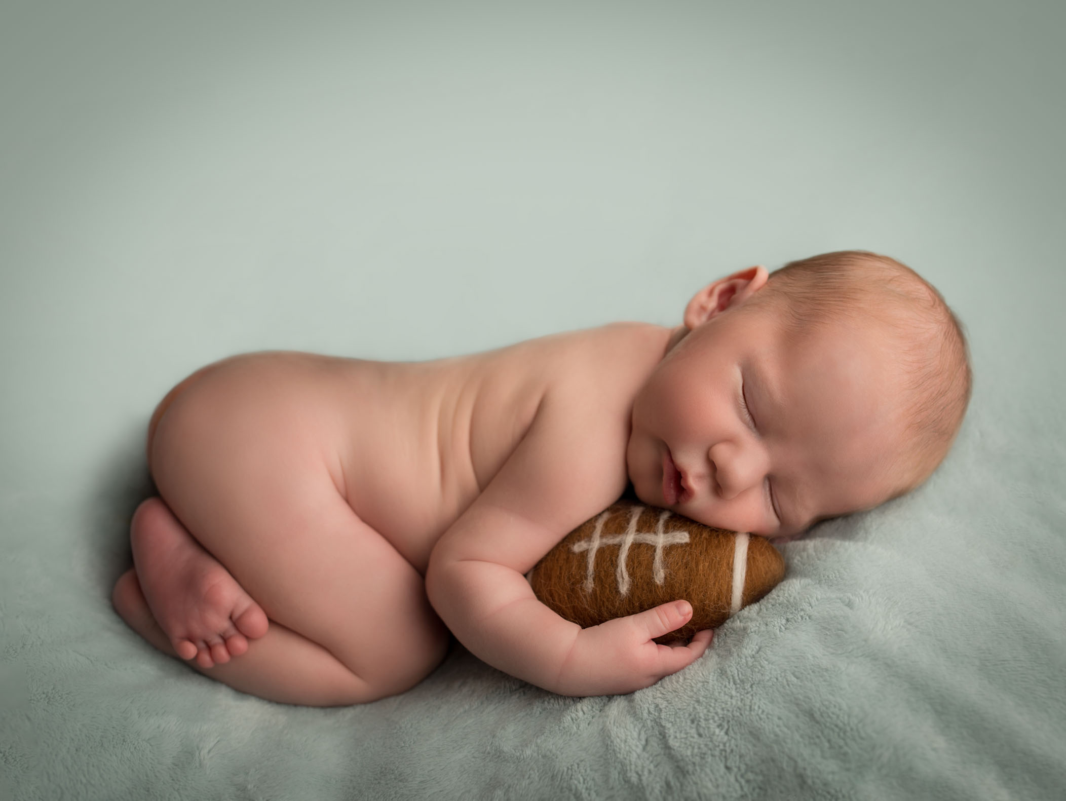 newborn baby boy cuddling football