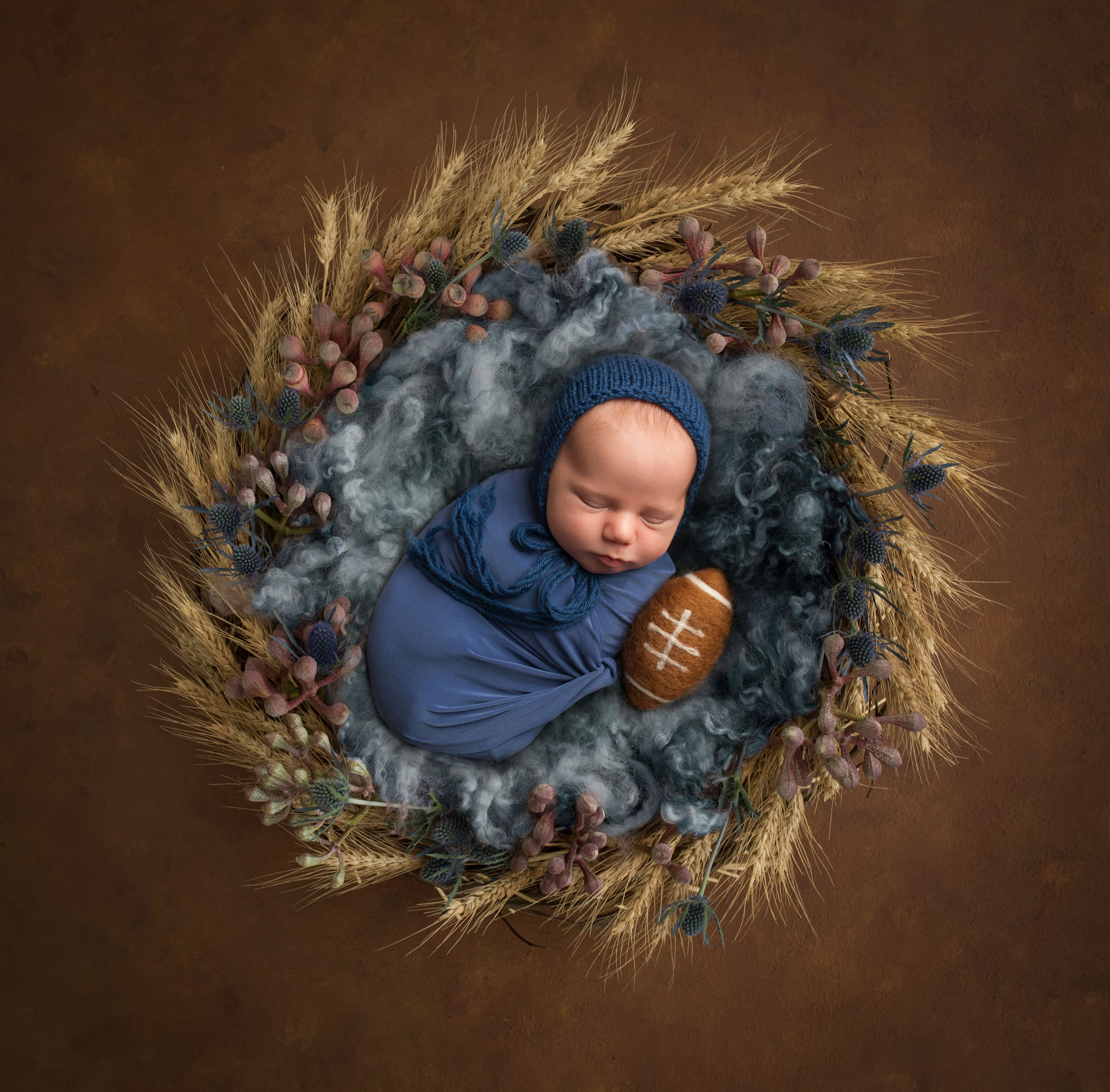 newborn baby boy swaddled in blue in wreath with football
