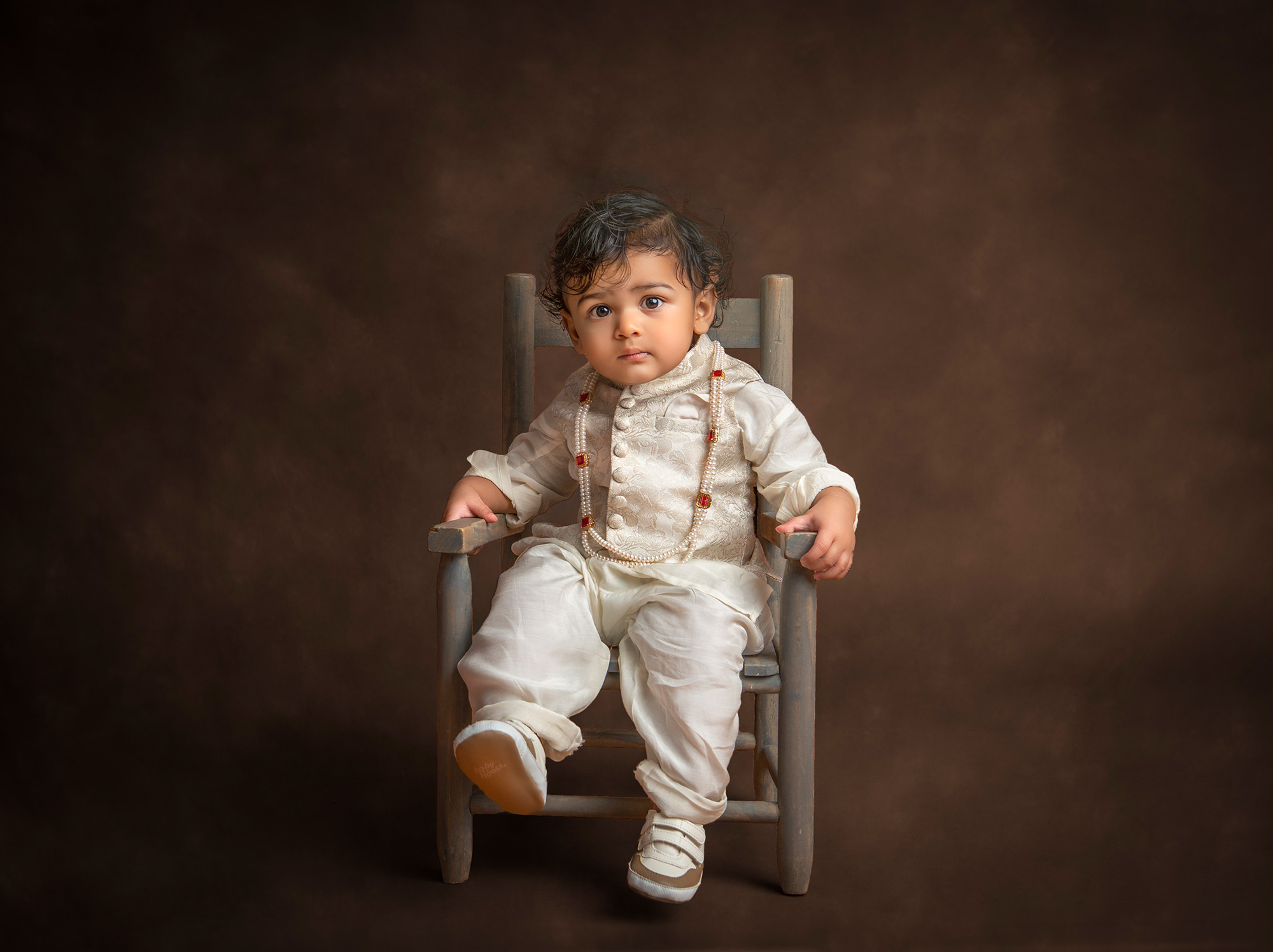 in studio family photos 1 year old indian boy dressed in traditional indian attire sitting in a toddler-size chair