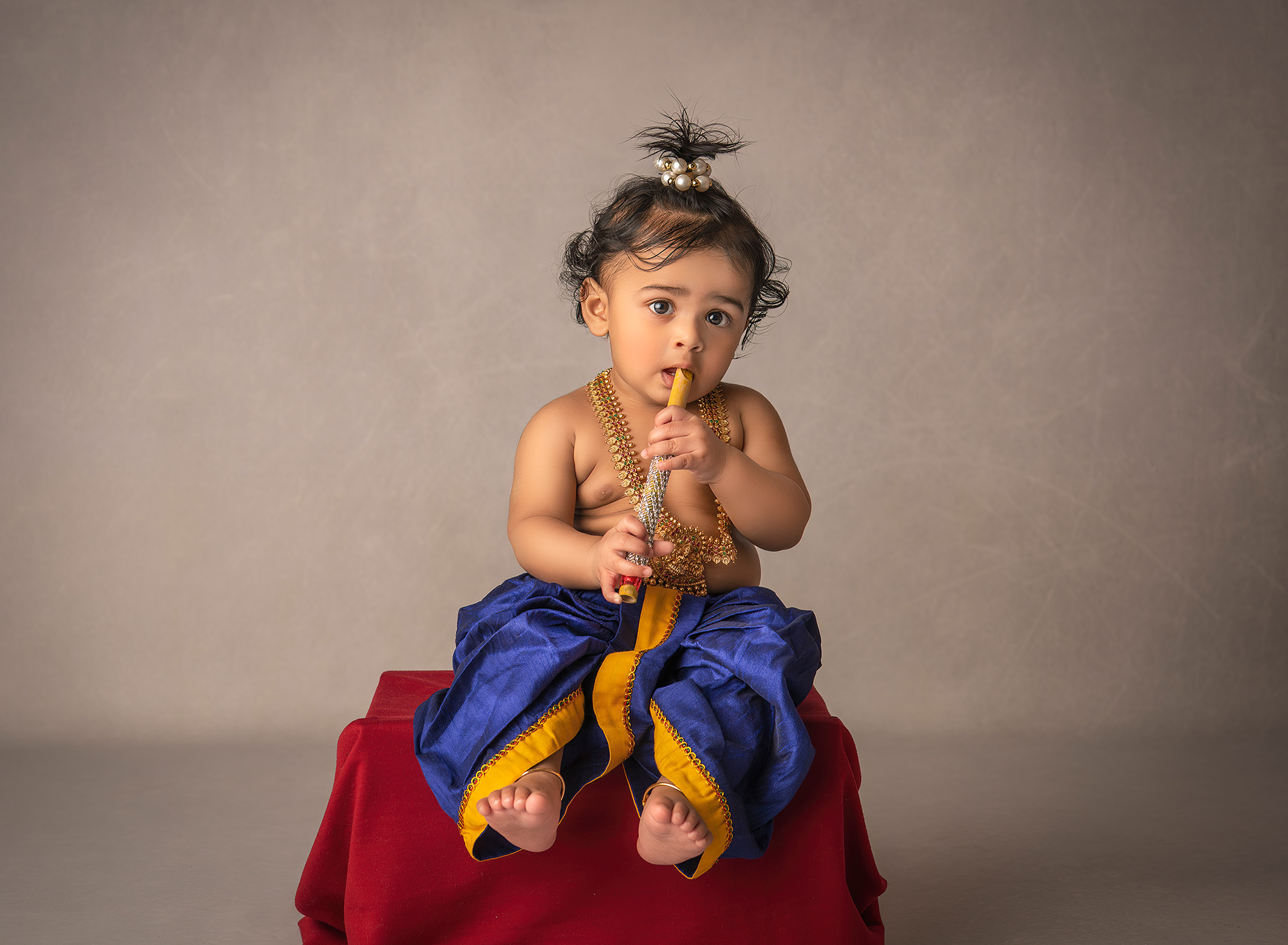 1 year old indian boy dressed as baby Krishna playing a flute