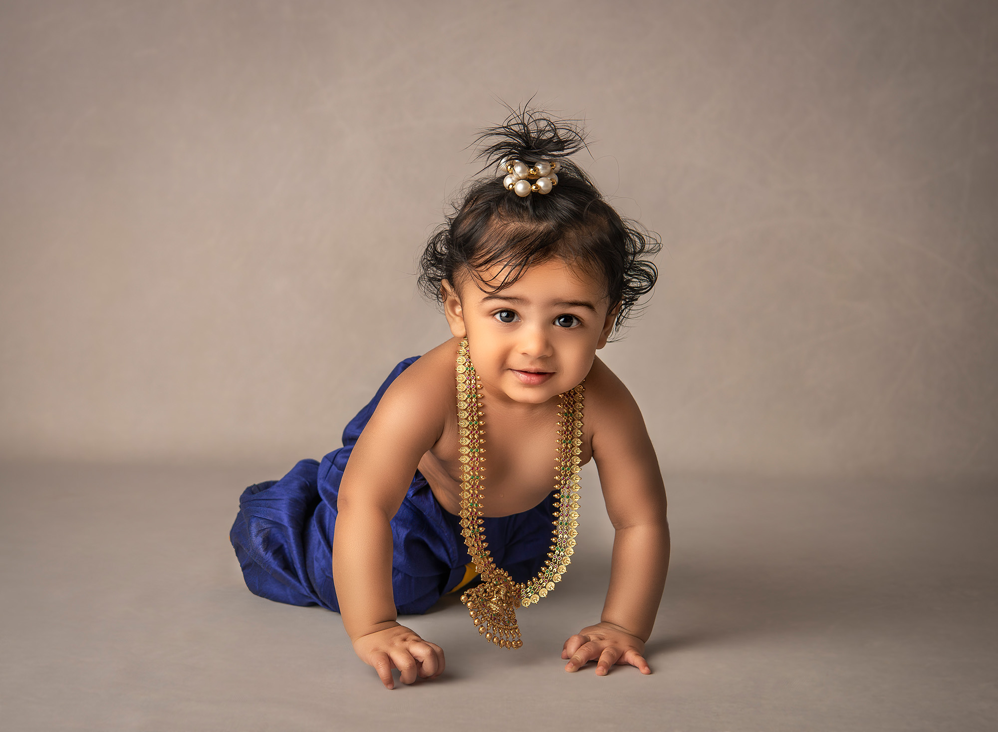 1 year old indian boy dressed as baby Krishna wearing a long gold necklace crawling