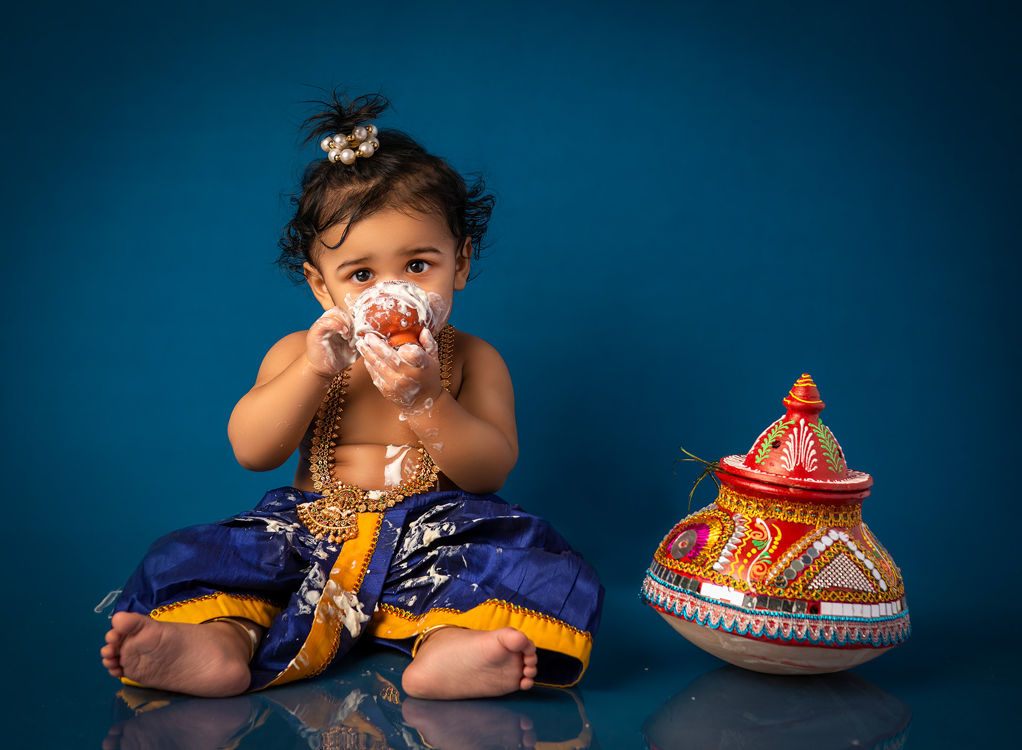 1 year old indian boy dressed as baby Krishna eating a cup of yogurt