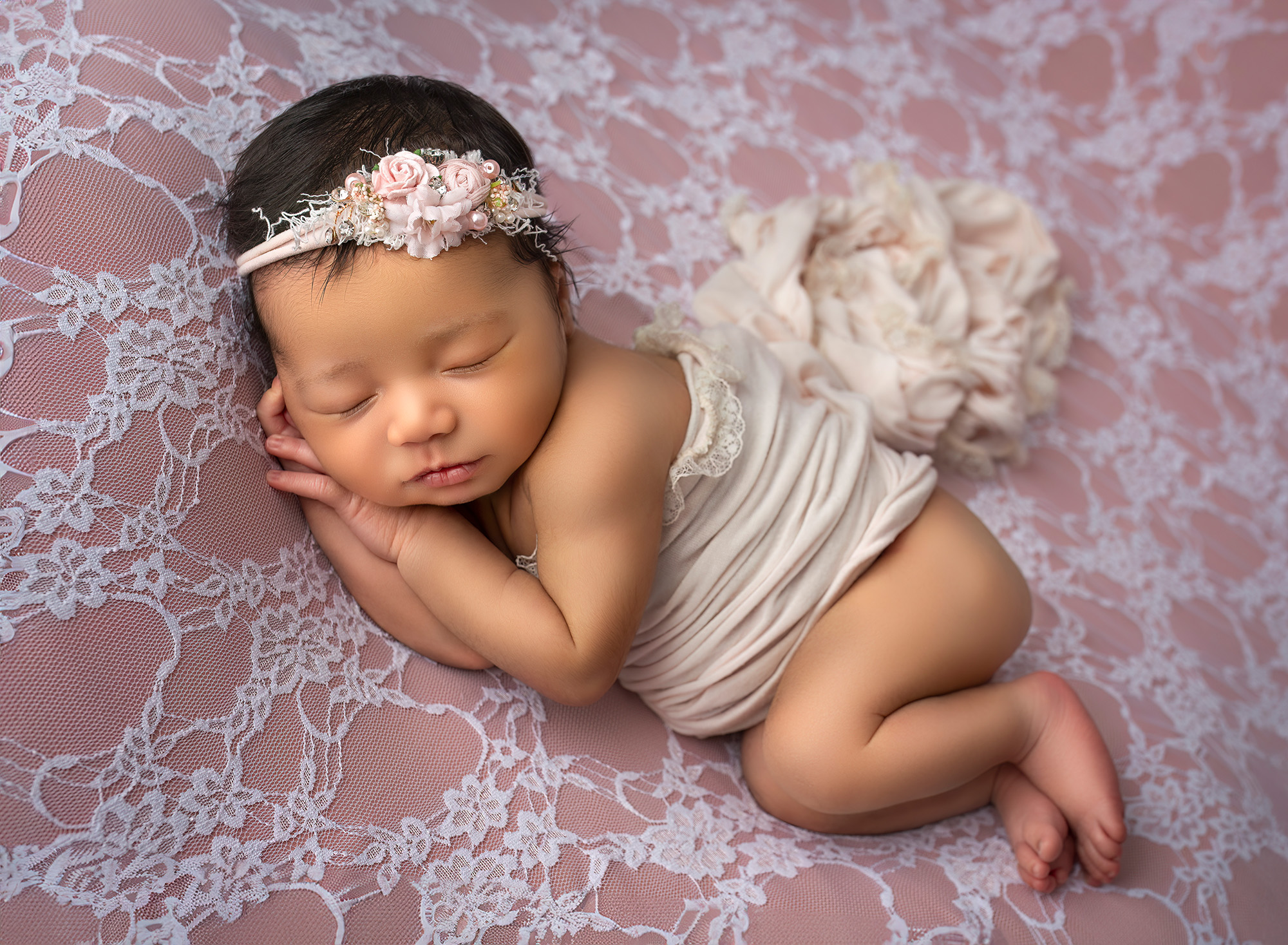 newborn baby girl asleep resting head on her hands on peach lace backdrop