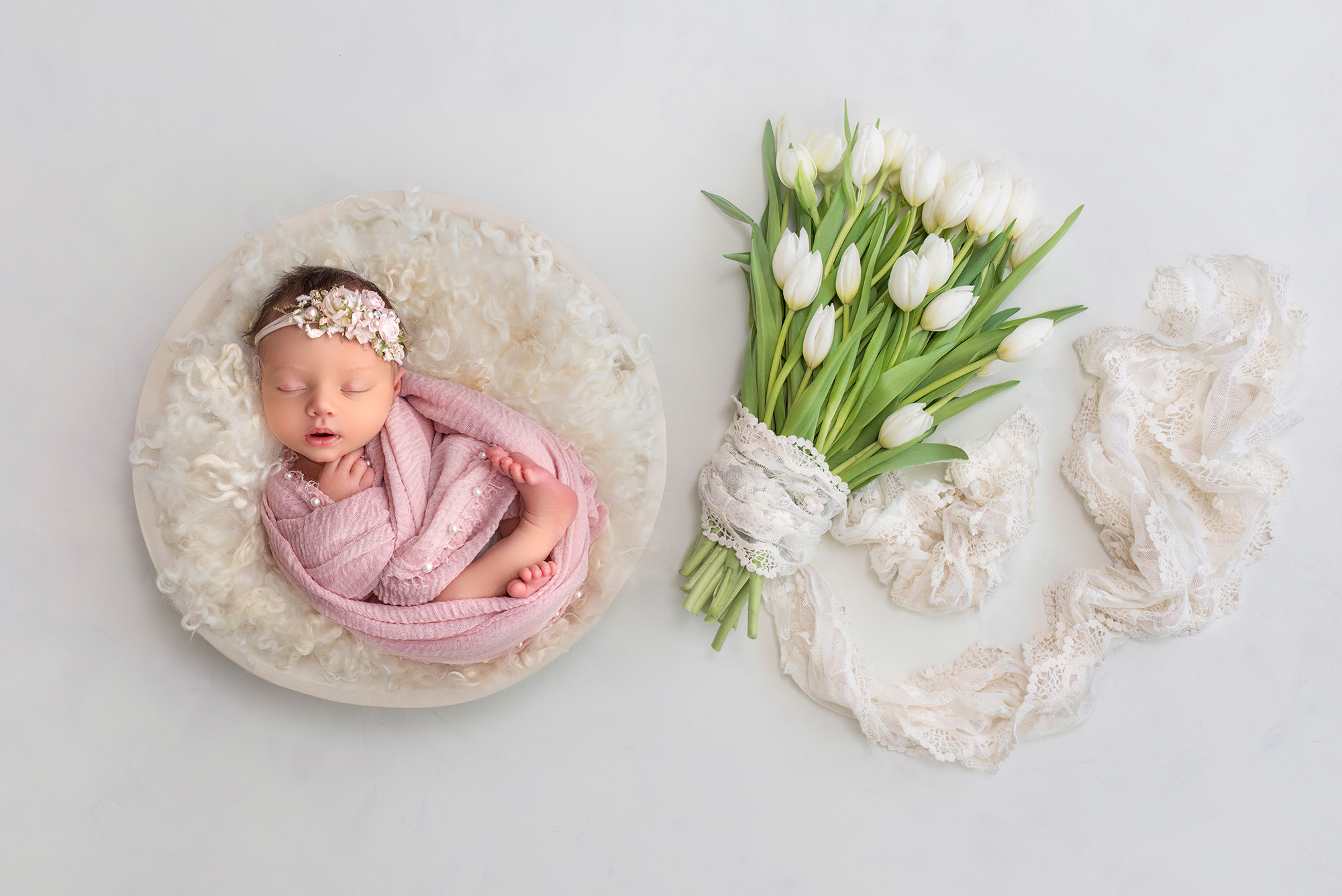 Brooklyn in a white bowl with a bouquet of white tulips lying next to her. 