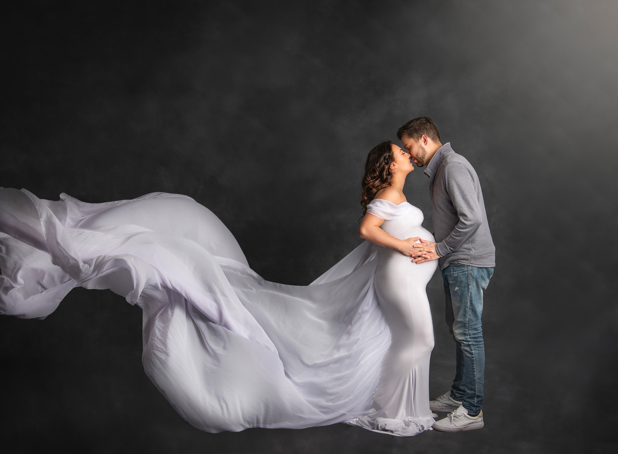 maternity and newborn photography Mom and Dad sharing a kiss, with her white flowing maternity dress floating through the frame. 