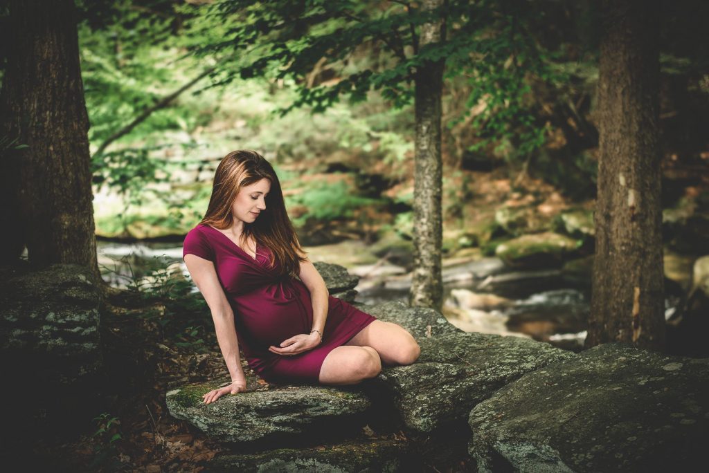 maternity picture pregnant mom standing in river with rocks and sun beams One Big Happy Photo