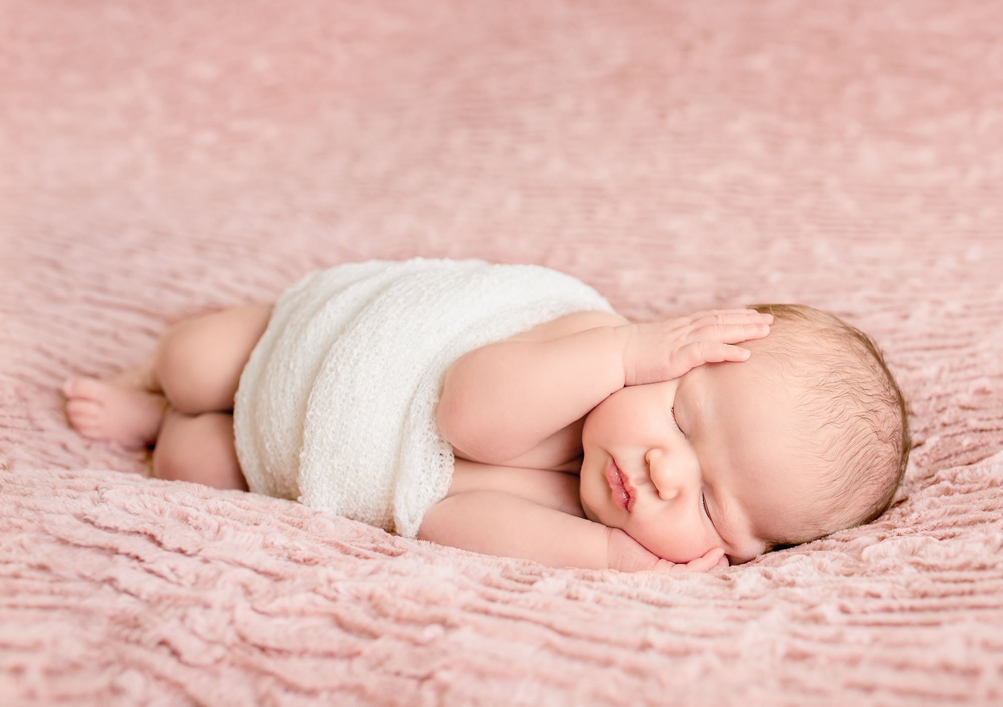 neborn baby girl wrapped in cream sleeping on pink with both hands on cheeks One Big Happy Photo