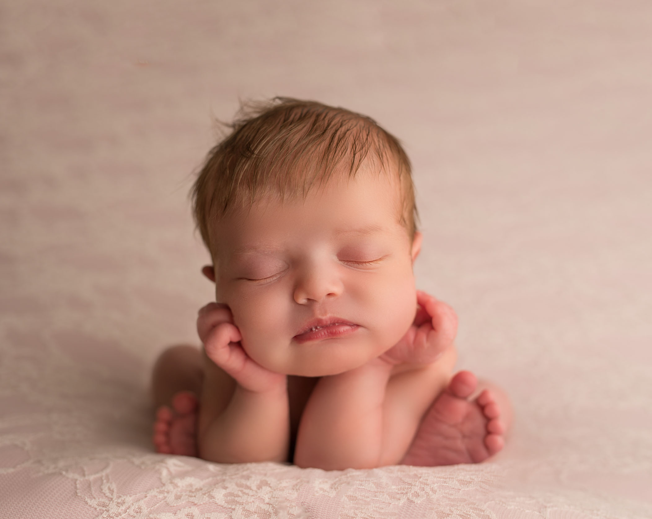 newborn baby in froggy position on pink background