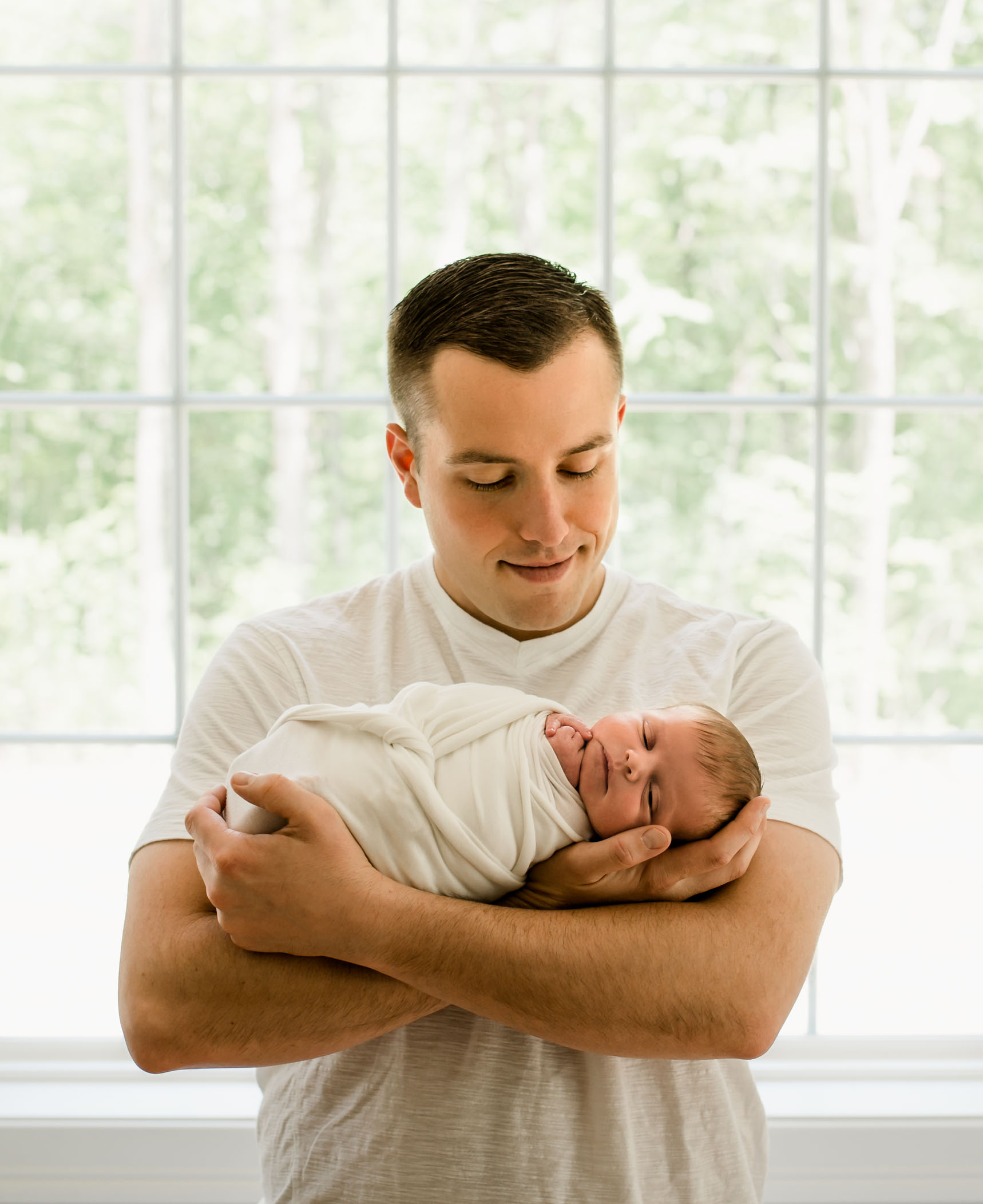Dad holding baby in his arms in front of window