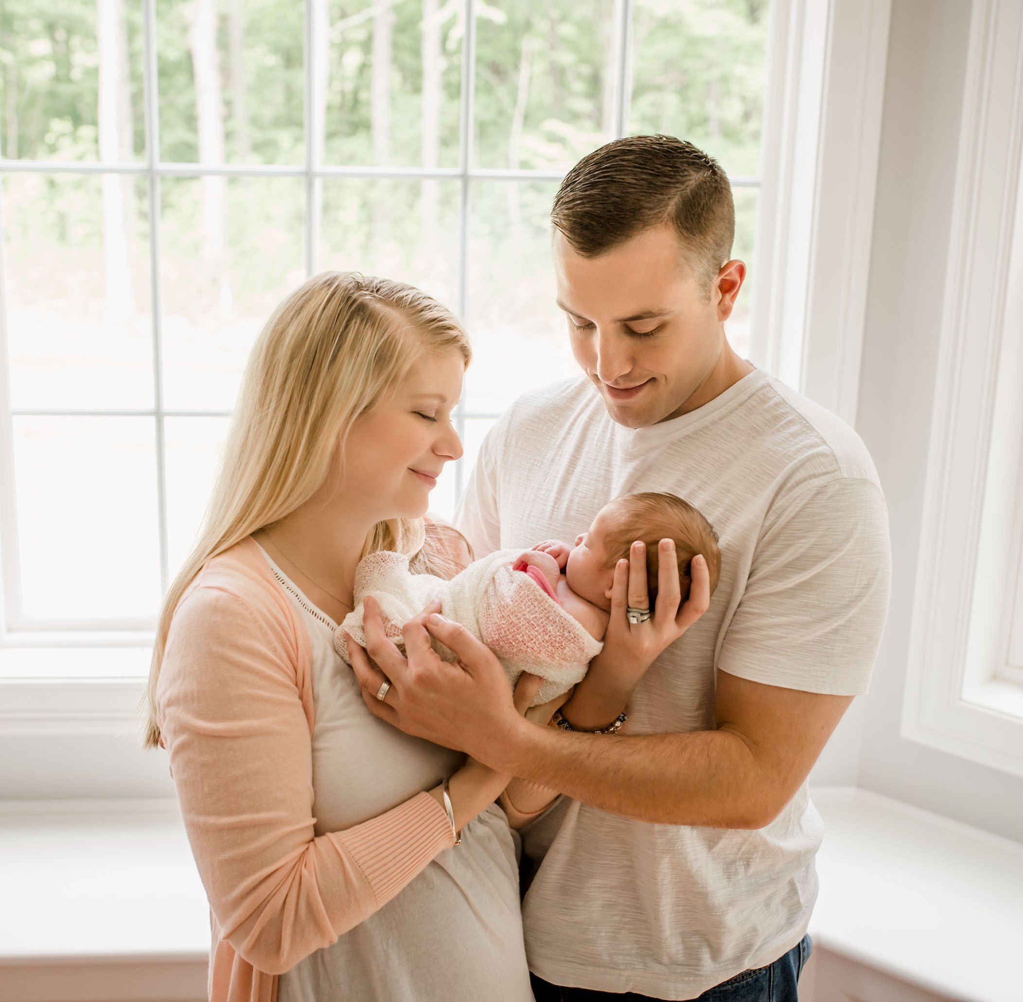 Mom & Dad hold baby girl in front of big picture window