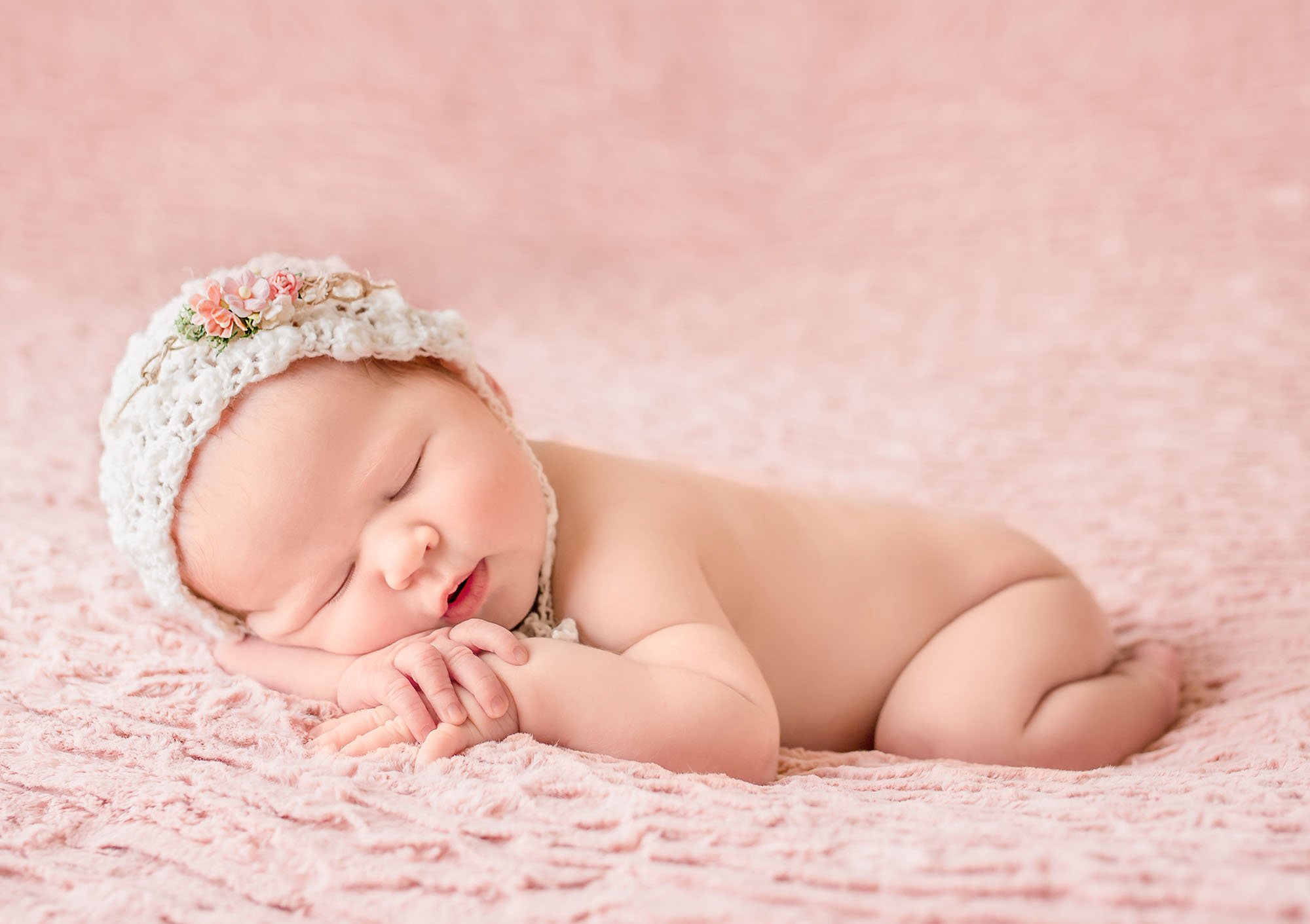 newborn baby girl sleeping with hands under cheek knitted bonnet with flowers One Big Happy Photo