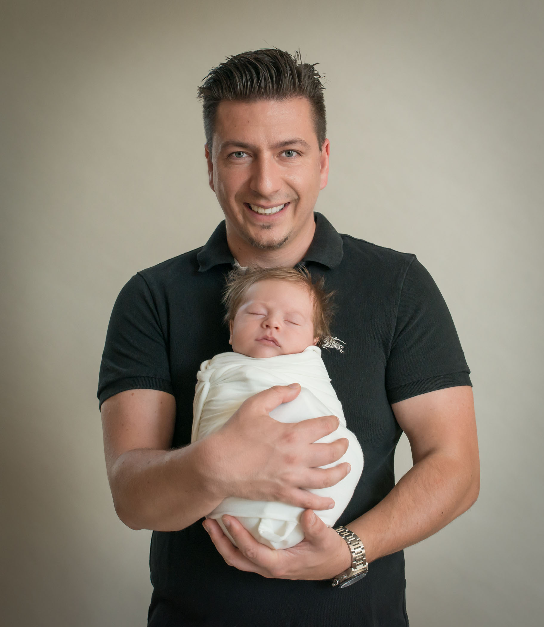 Dad smiling and holding wrapped newborn son against his chest