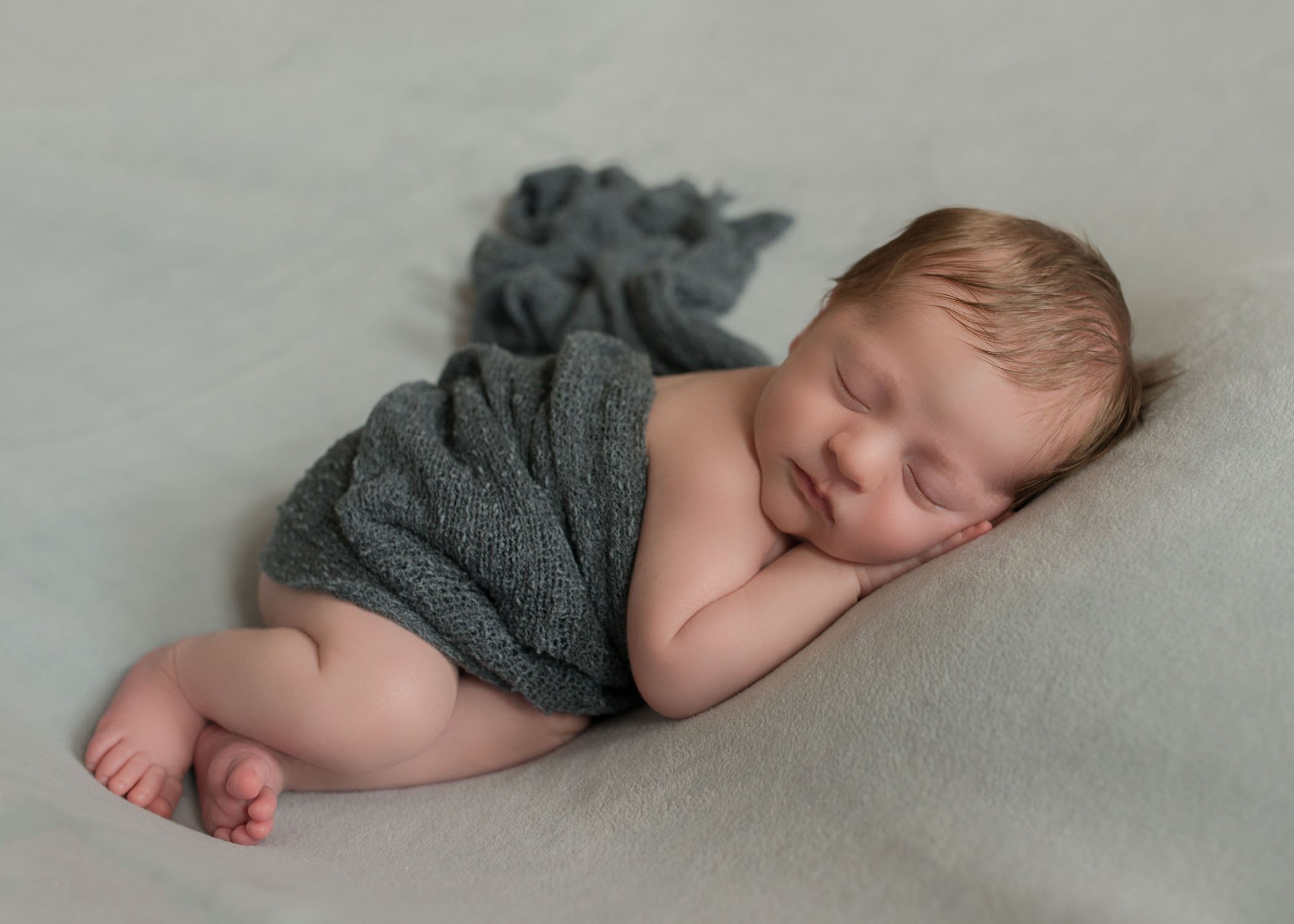 newborn baby boy sleeping on light grey on side with dark grey wrap