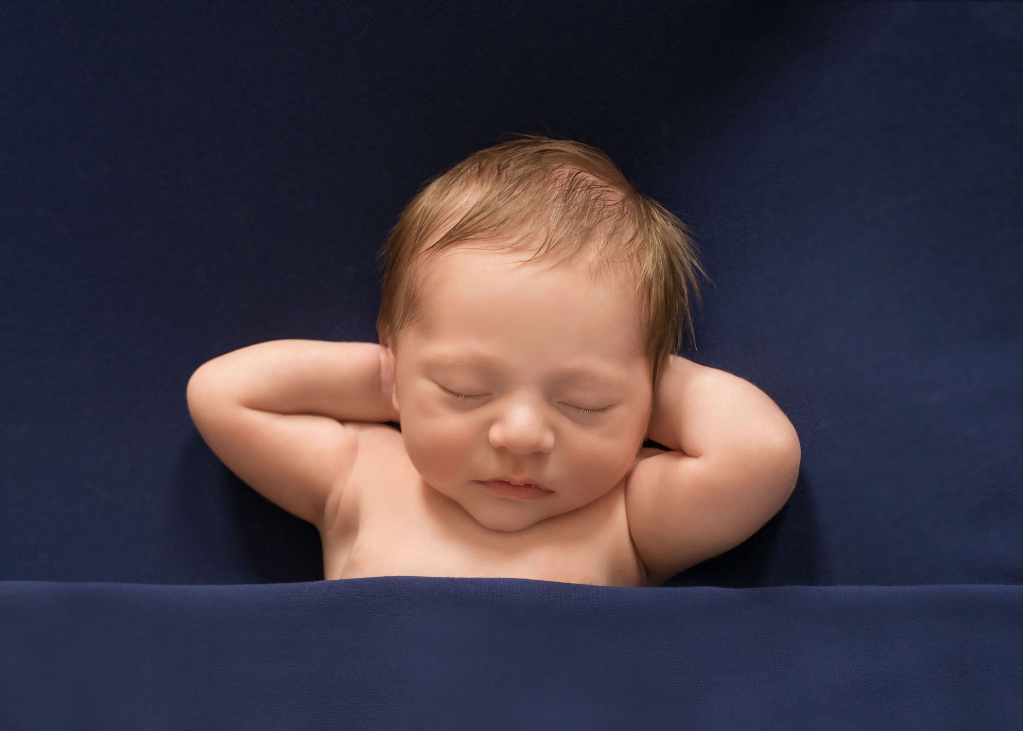 newborn baby boy sleeping with arms behind his head on blue