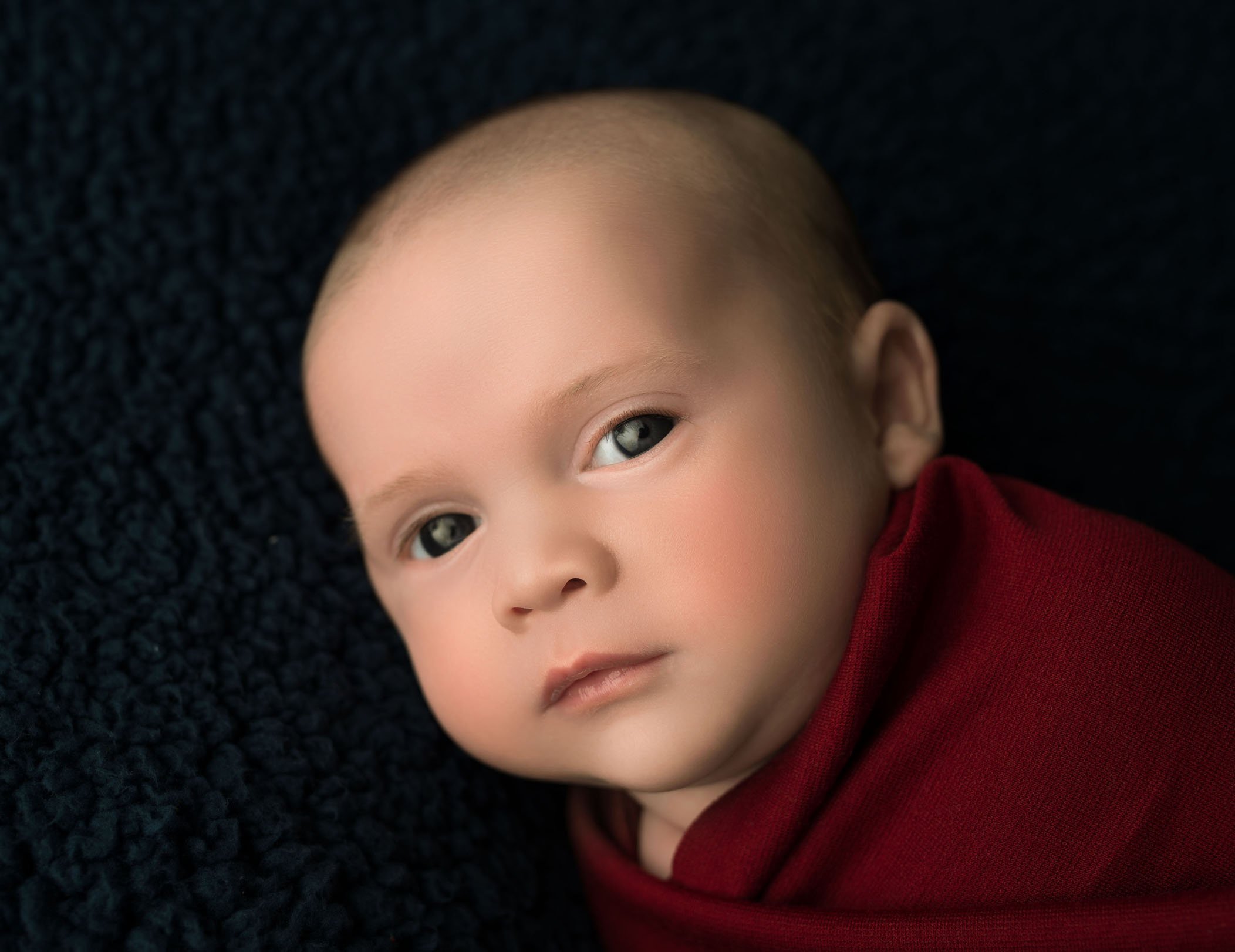 baby boy wrapped in red on dark blue with eyes open