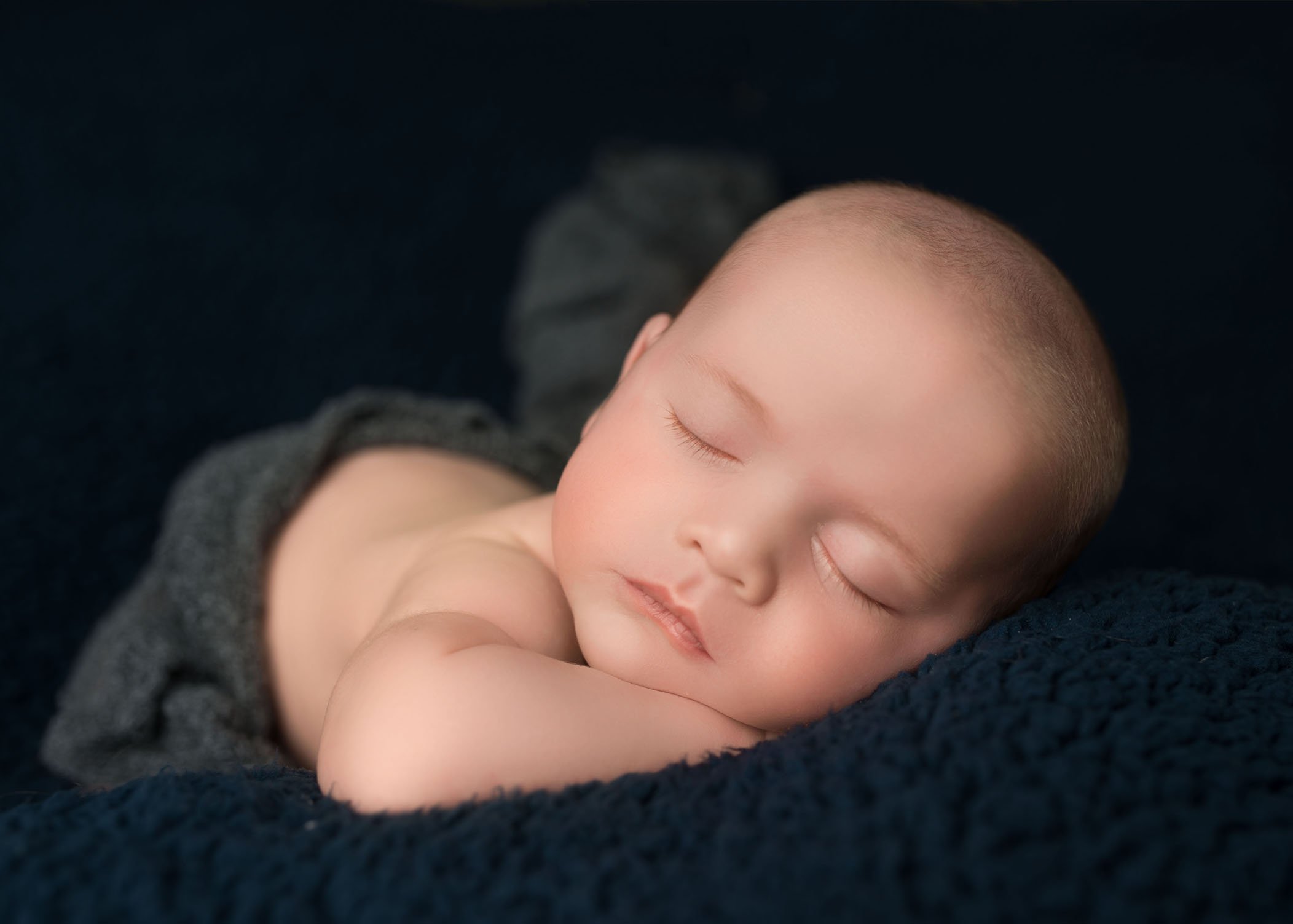 newborn baby boy sleeping on side on dark blue with eyelashes