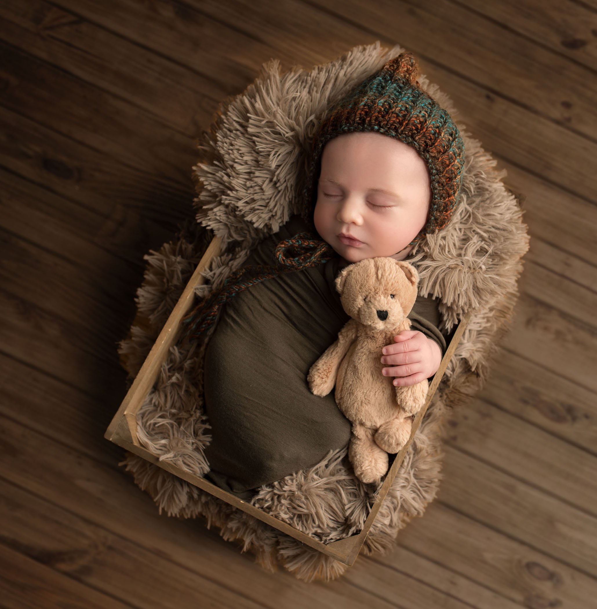 newborn baby boy sleeping in crate with teddy bear