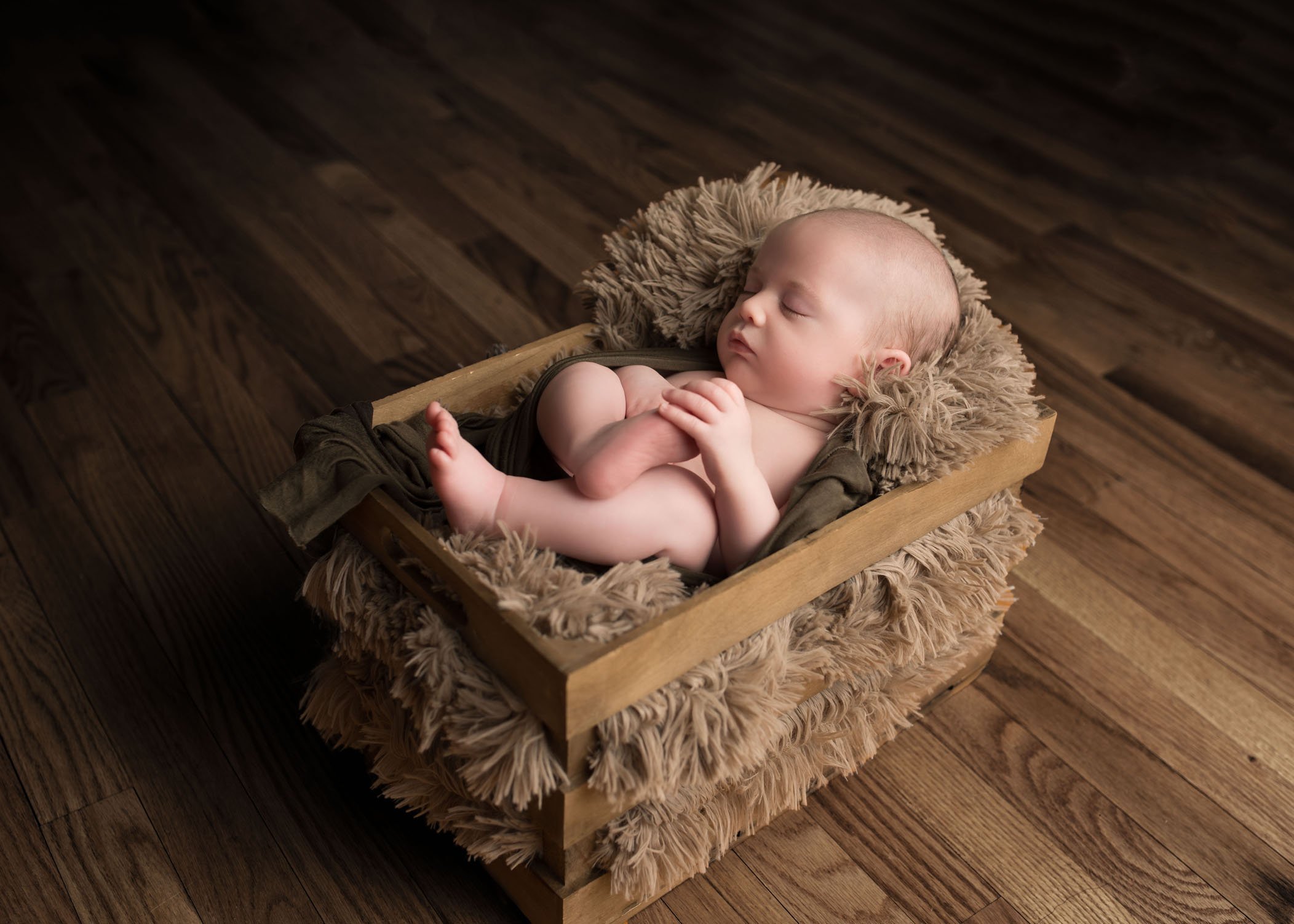 Newborn baby boy sleeping in crate with fur