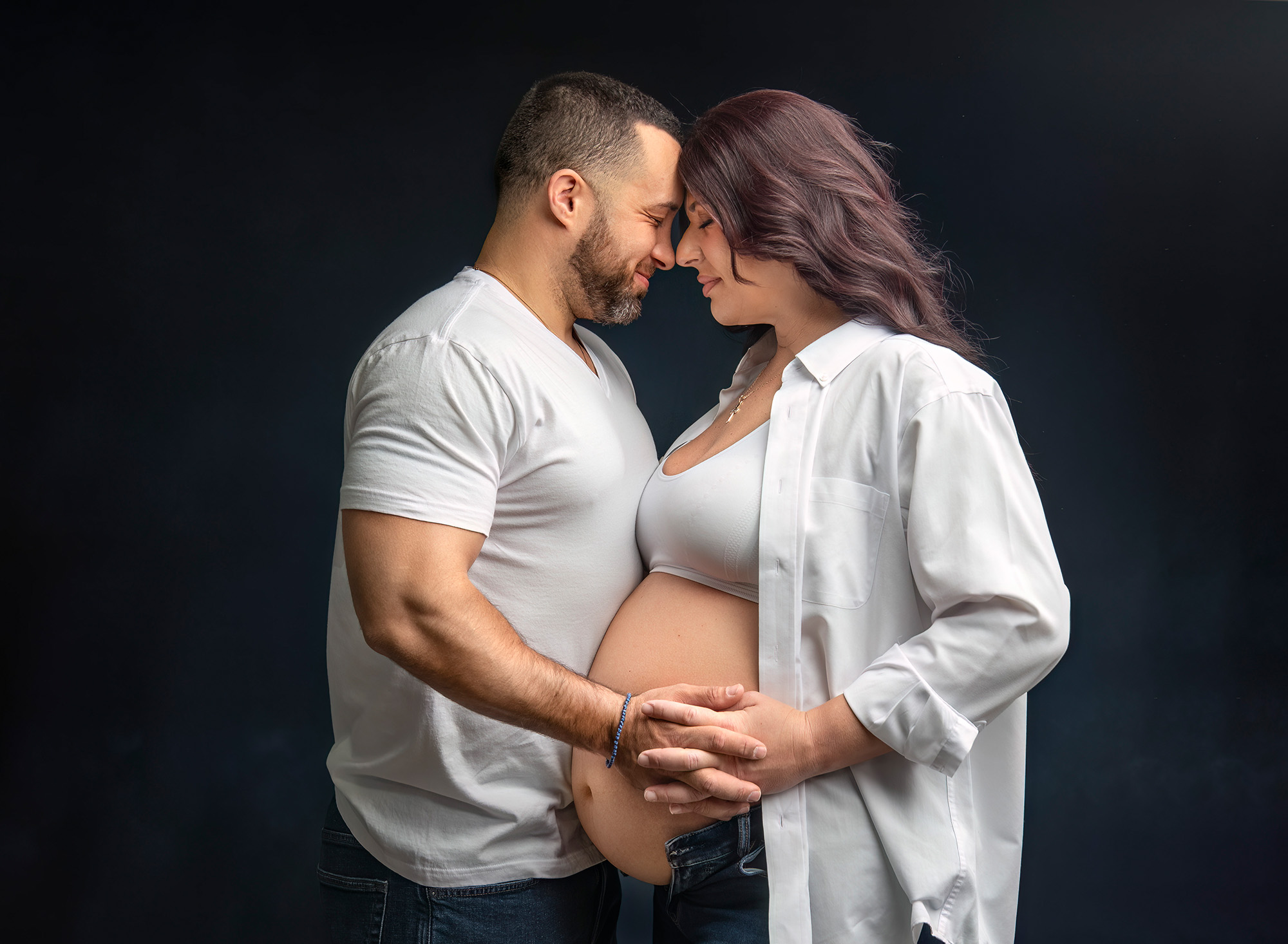 Newborn Maternity Photographer mom and dad facing each other with the fingers intertwined in front of mom's growing belly.