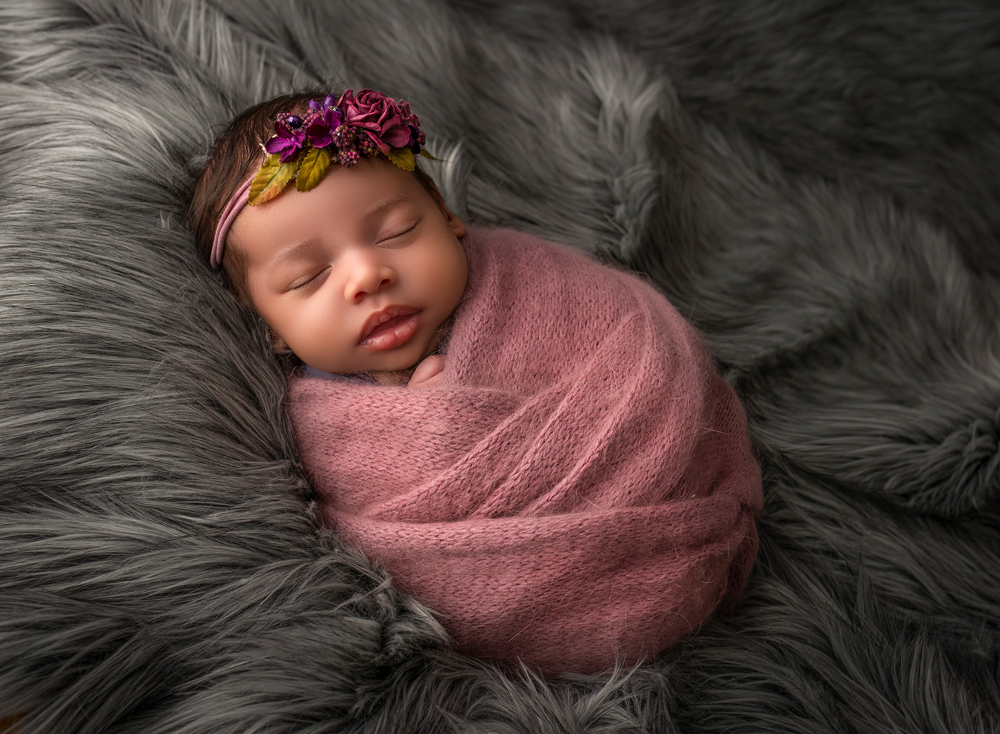 newborn baby girl wrapped in pink blanket asleep on grey fur background