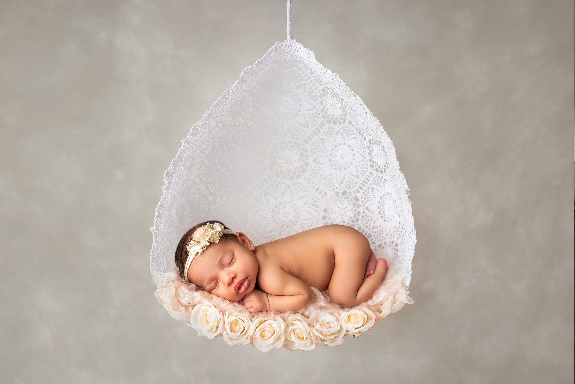 newborn baby girl asleep in a teardrop swing with pale pink roses