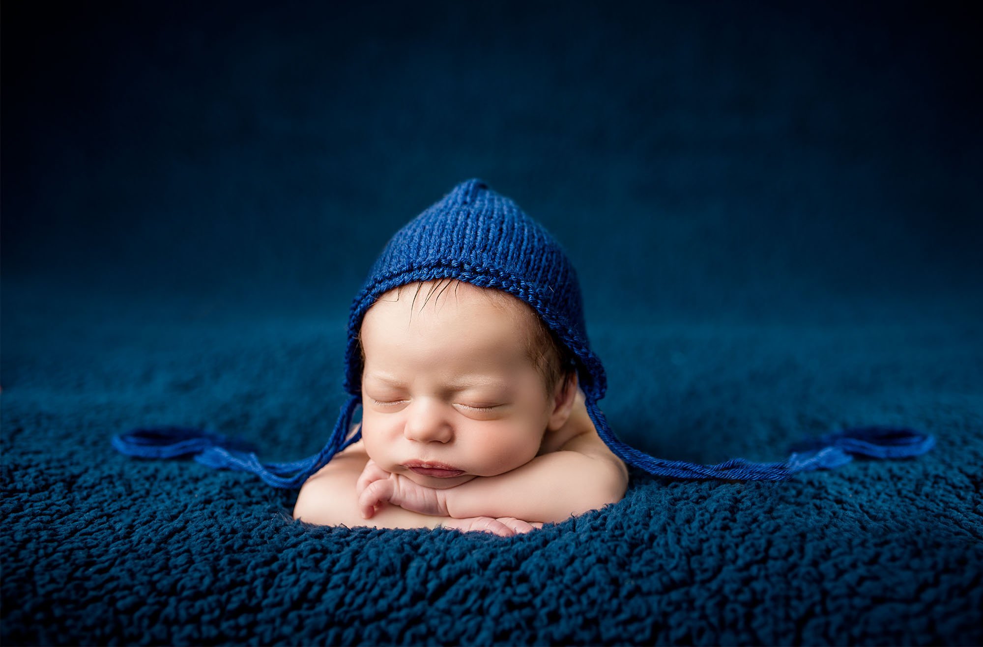 newborn baby boy sleeping on blue blanket with head on hands and blue knit cap