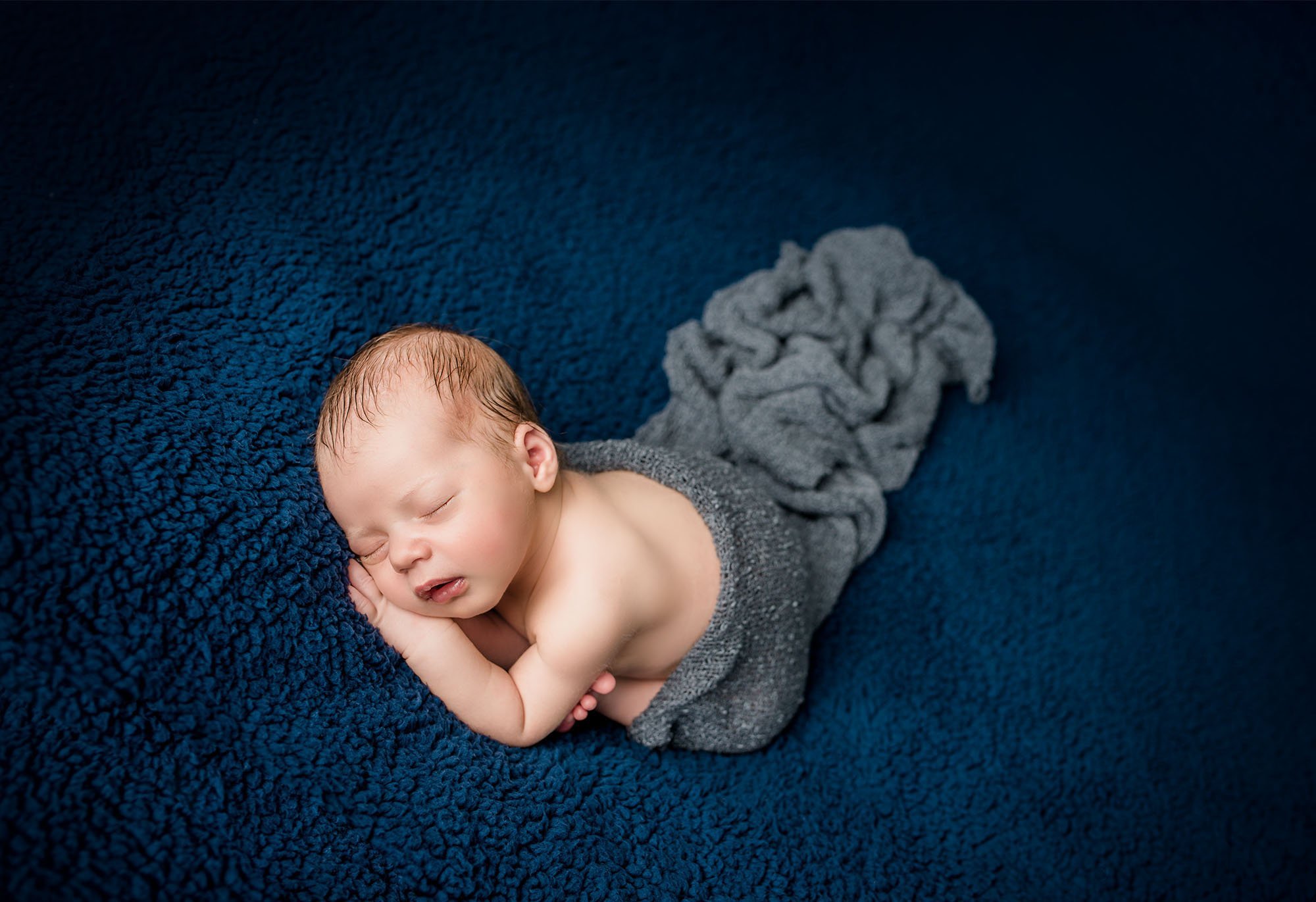 newborn baby sleeping on blue blanket with grey wrap