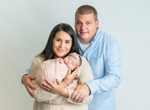 new parents cradling newborn baby girl swaddled in peach