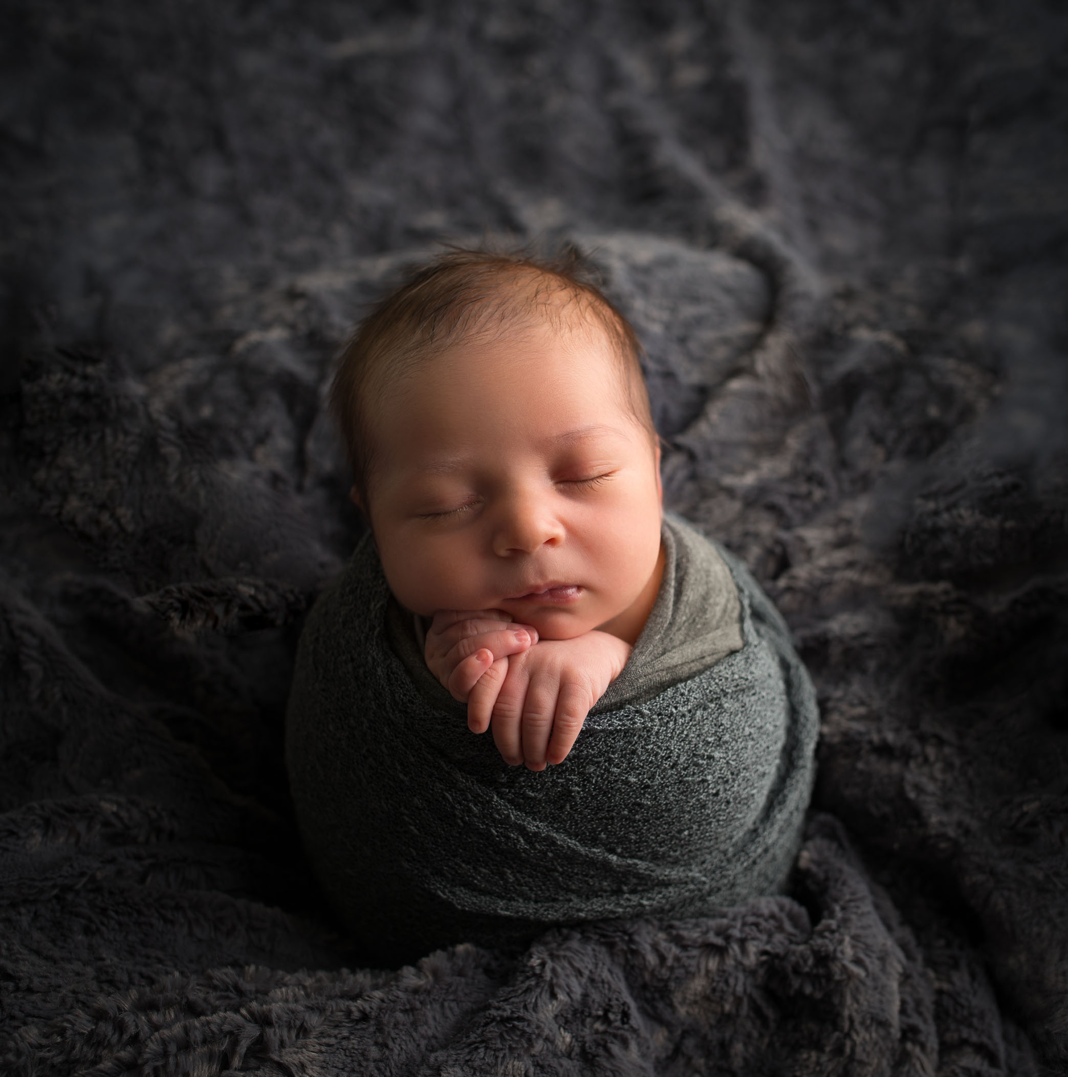 newborn baby in potato sack pose on dark grey background