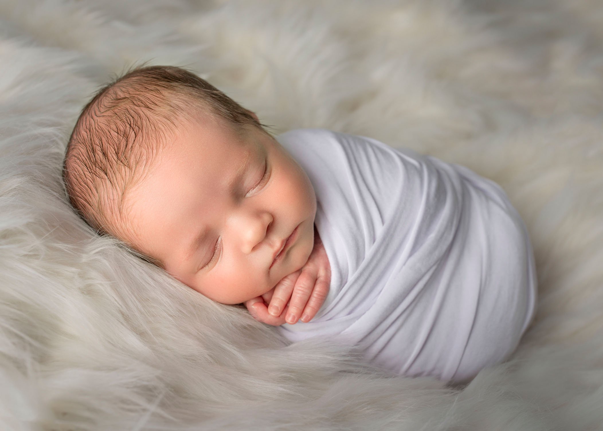 newborn baby boy sleeping wrapped in white on cream fur