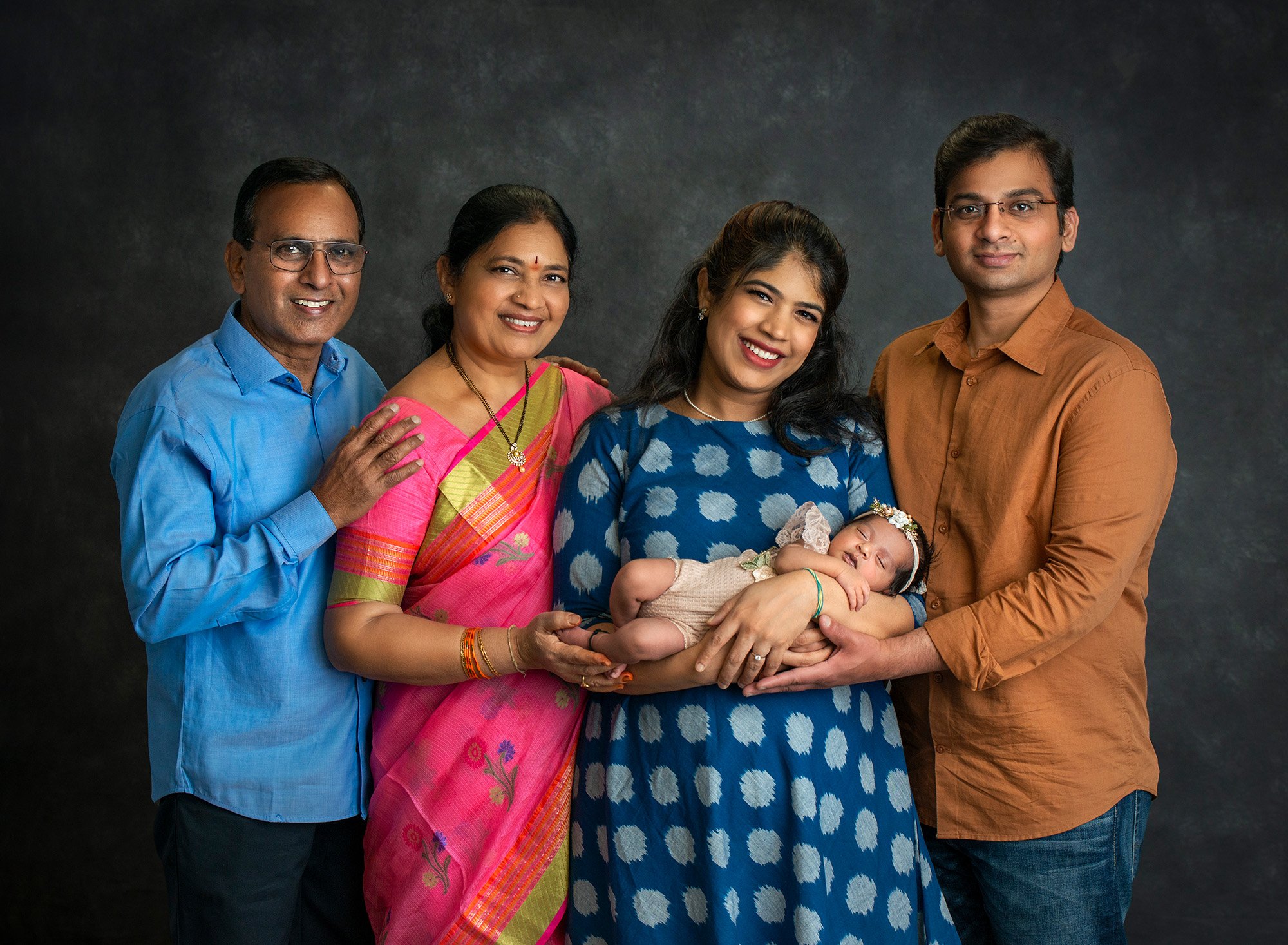 couple posing with parents cradling newborn baby girl